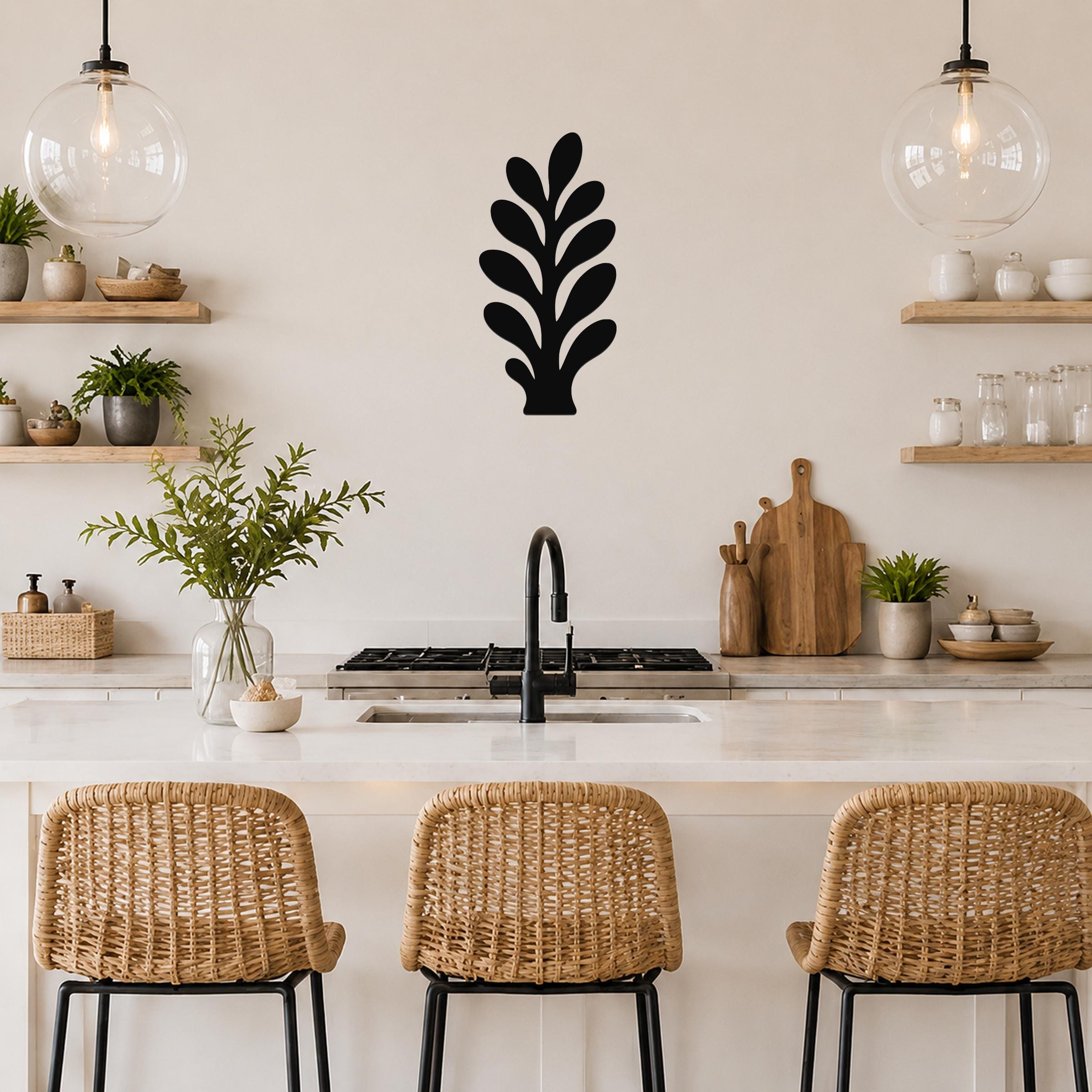 Black metal wall art in a leafy sprig silhouette, mounted on a kitchen wall above a counter with wicker bar stools.