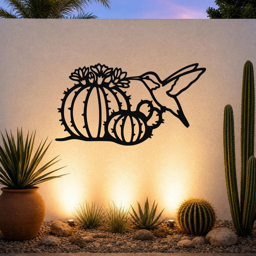 Black metal wall art featuring a hummingbird and barrel cactus with flower cutouts, mounted on an outdoor wall above a desert garden with potted plants and ground lights.