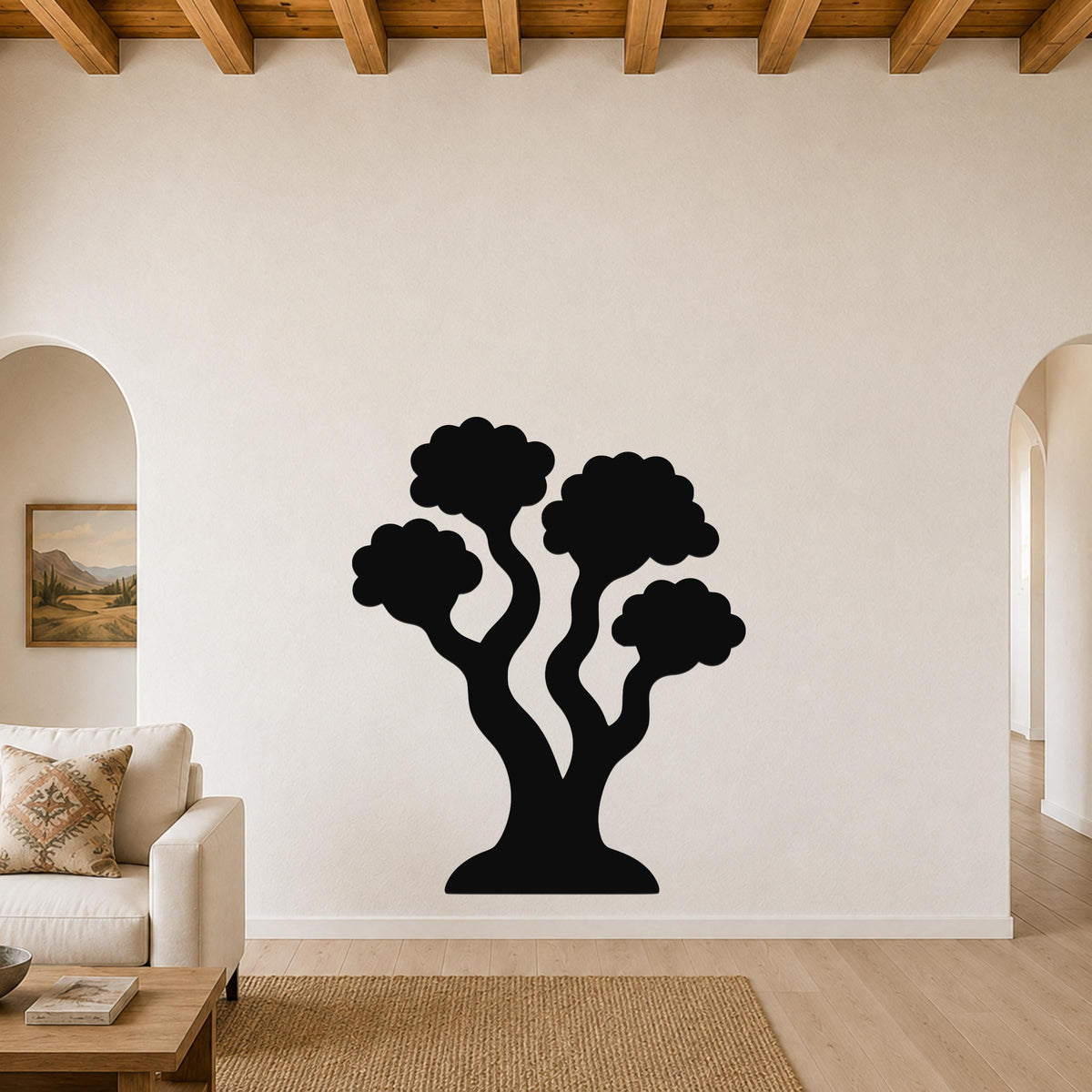 Black metal tree wall art with a silhouette design of three rounded canopies and curved trunks, mounted on a living room wall above a sofa.