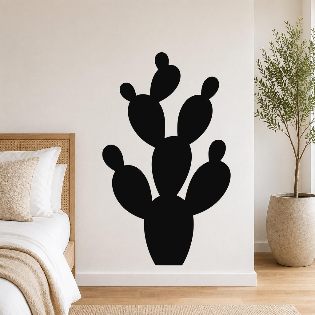 Black metal prickly pear cactus wall art with cutout segments, mounted on a bedroom wall above a bed.