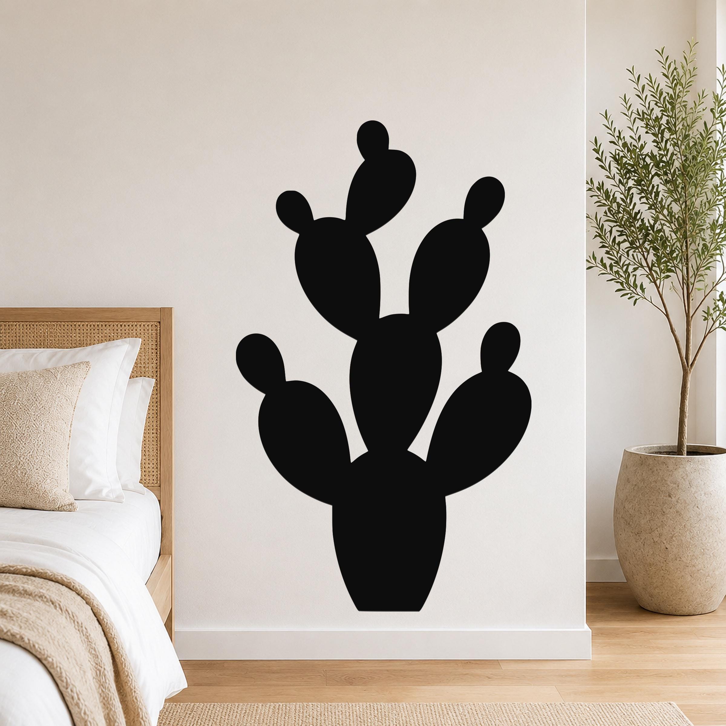 Black metal prickly pear cactus wall art with cutout segments, mounted on a bedroom wall above a bed.