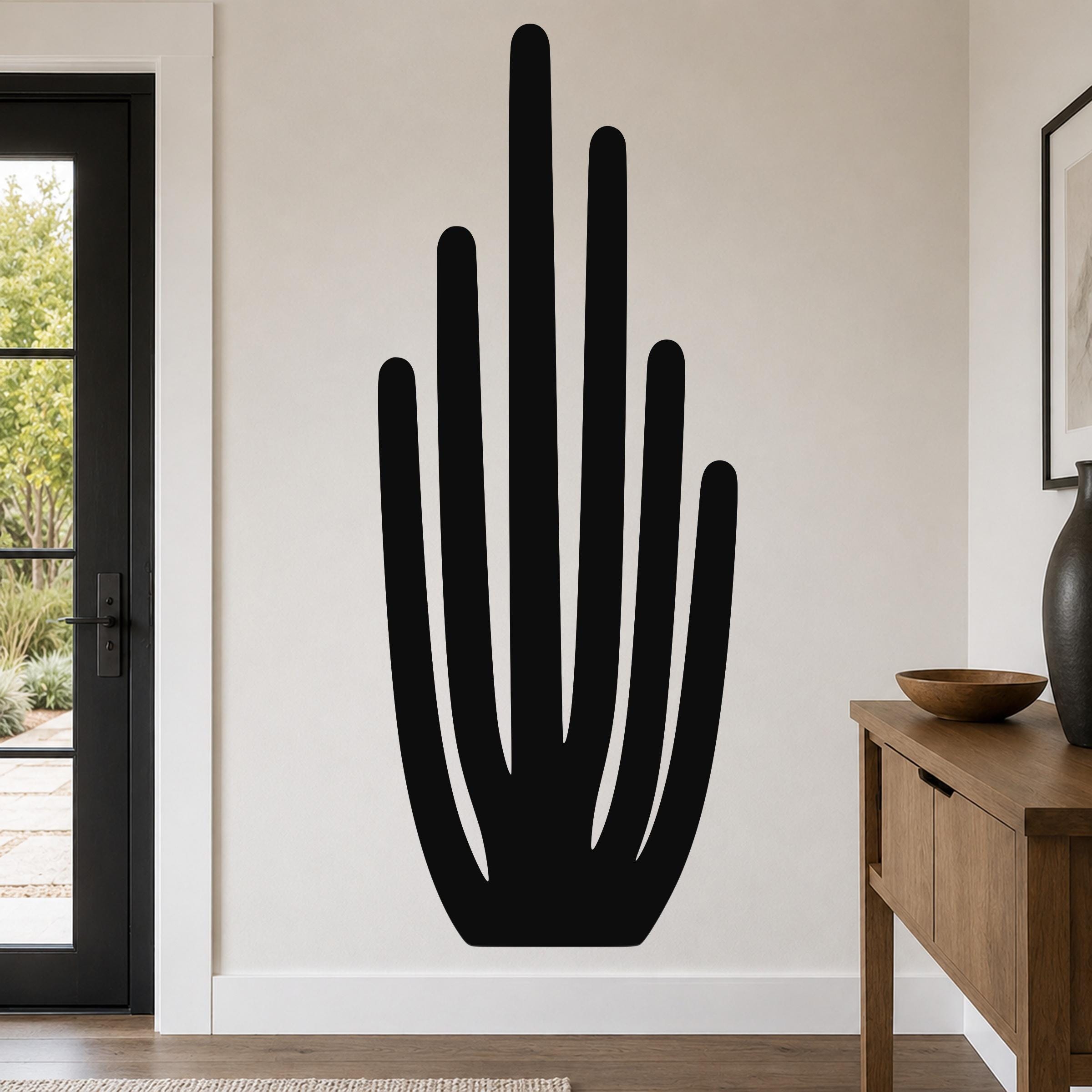 Black metal wall art in the shape of an organ pipe cactus with vertical spines, mounted on a living room wall above a wooden console table.