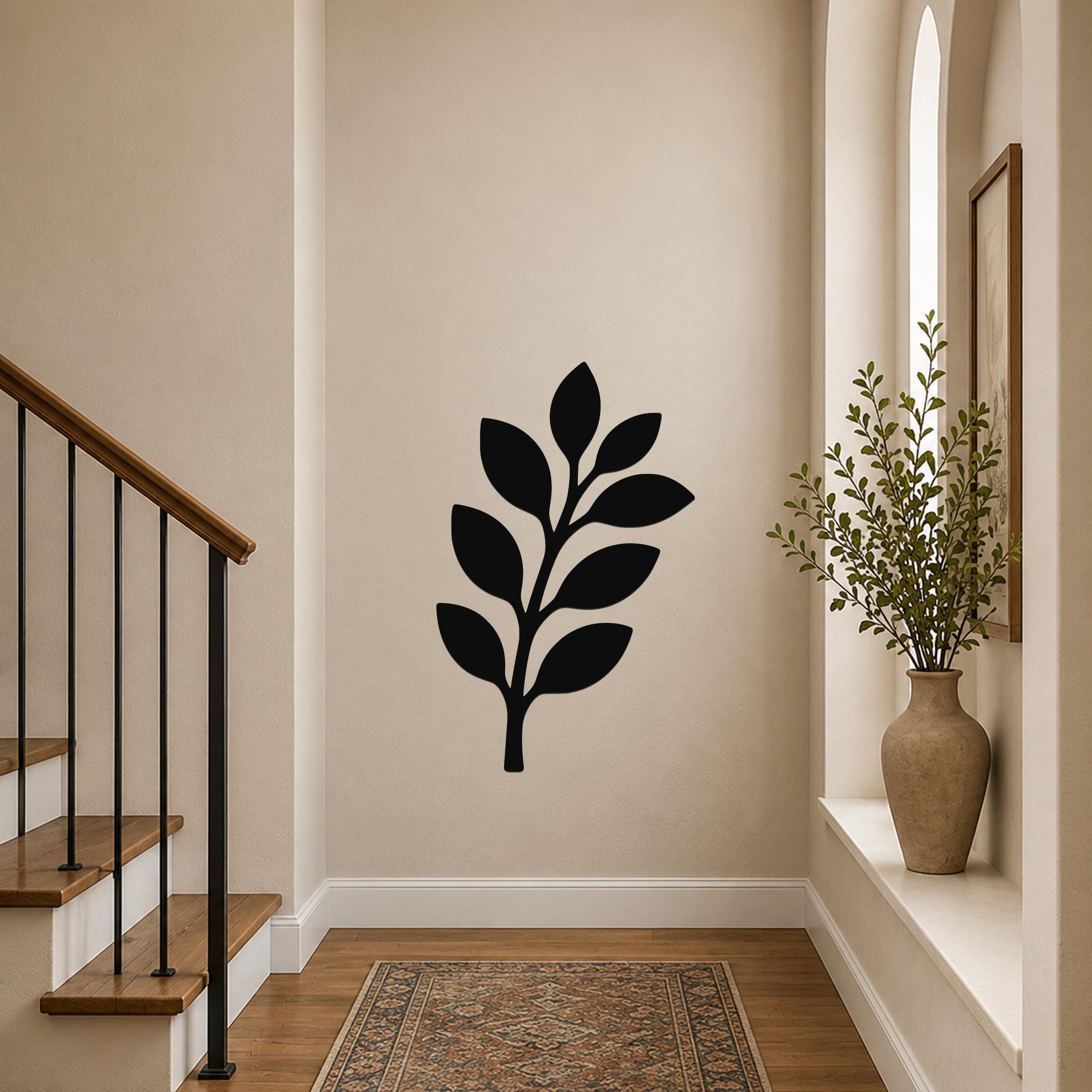 Black metal olive branch wall art with leaf cutouts, mounted on a hallway wall above a patterned rug near a staircase.