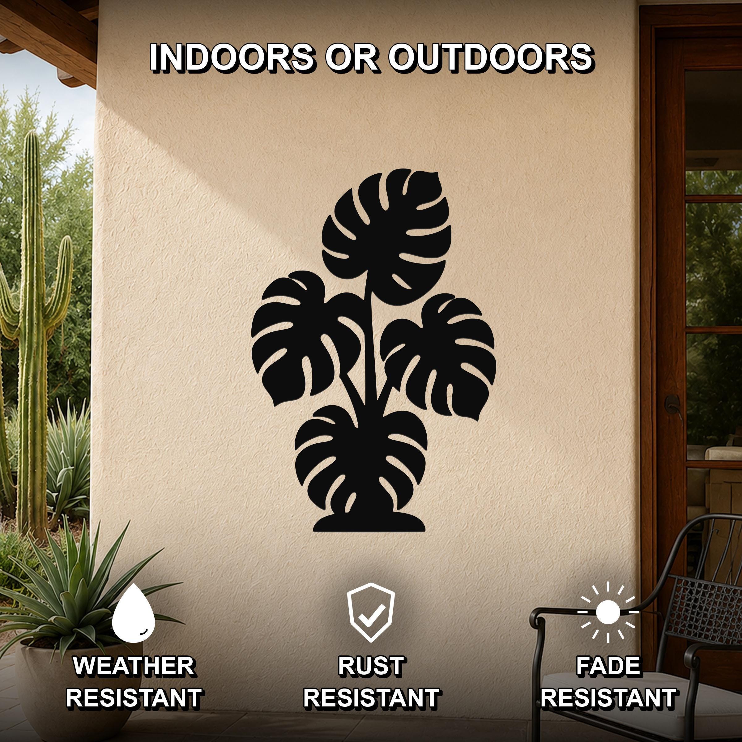 Black metal wall art featuring a monstera plant silhouette with cutout leaves, mounted on an outdoor patio wall above a potted plant.