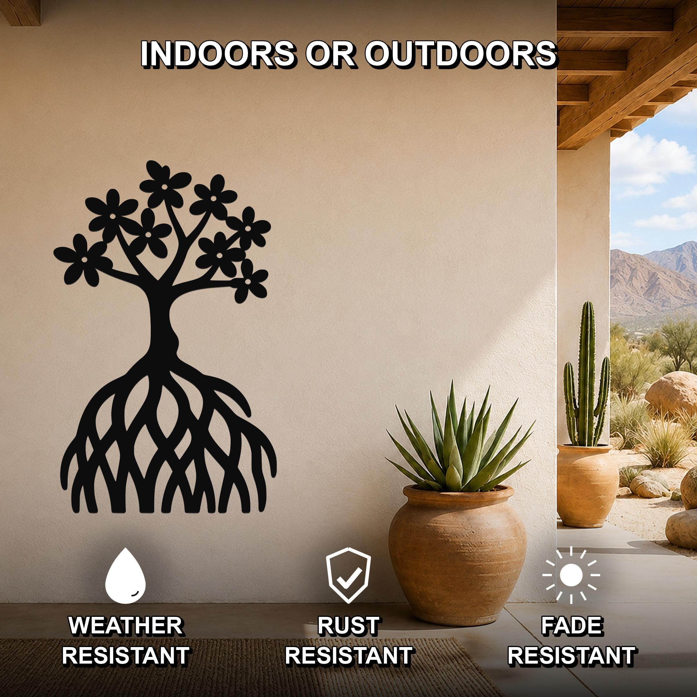 Black metal wall art shaped like a tree with flowers and visible roots, mounted on a beige outdoor wall beside potted plants.