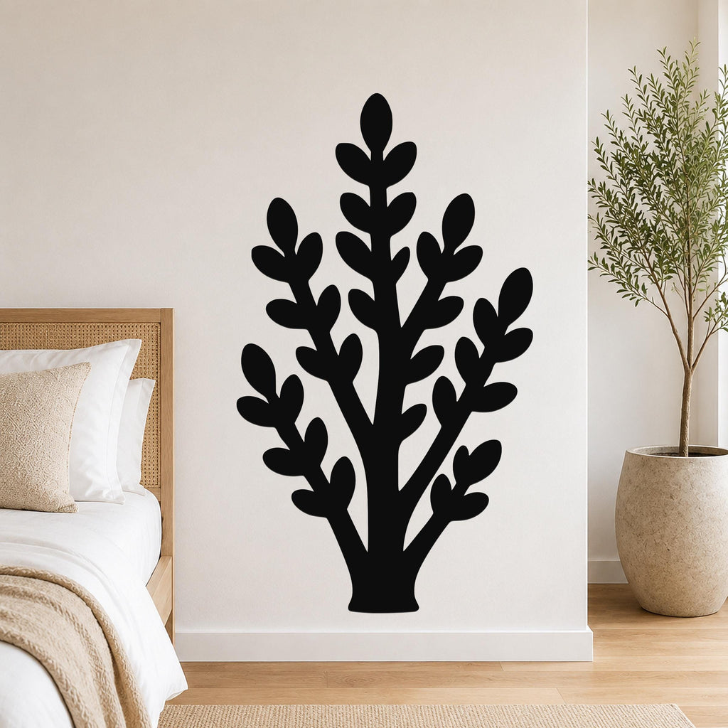 Black metal wall art in a silhouette of a leafy plant, mounted on a white bedroom wall above a bed with a woven headboard.