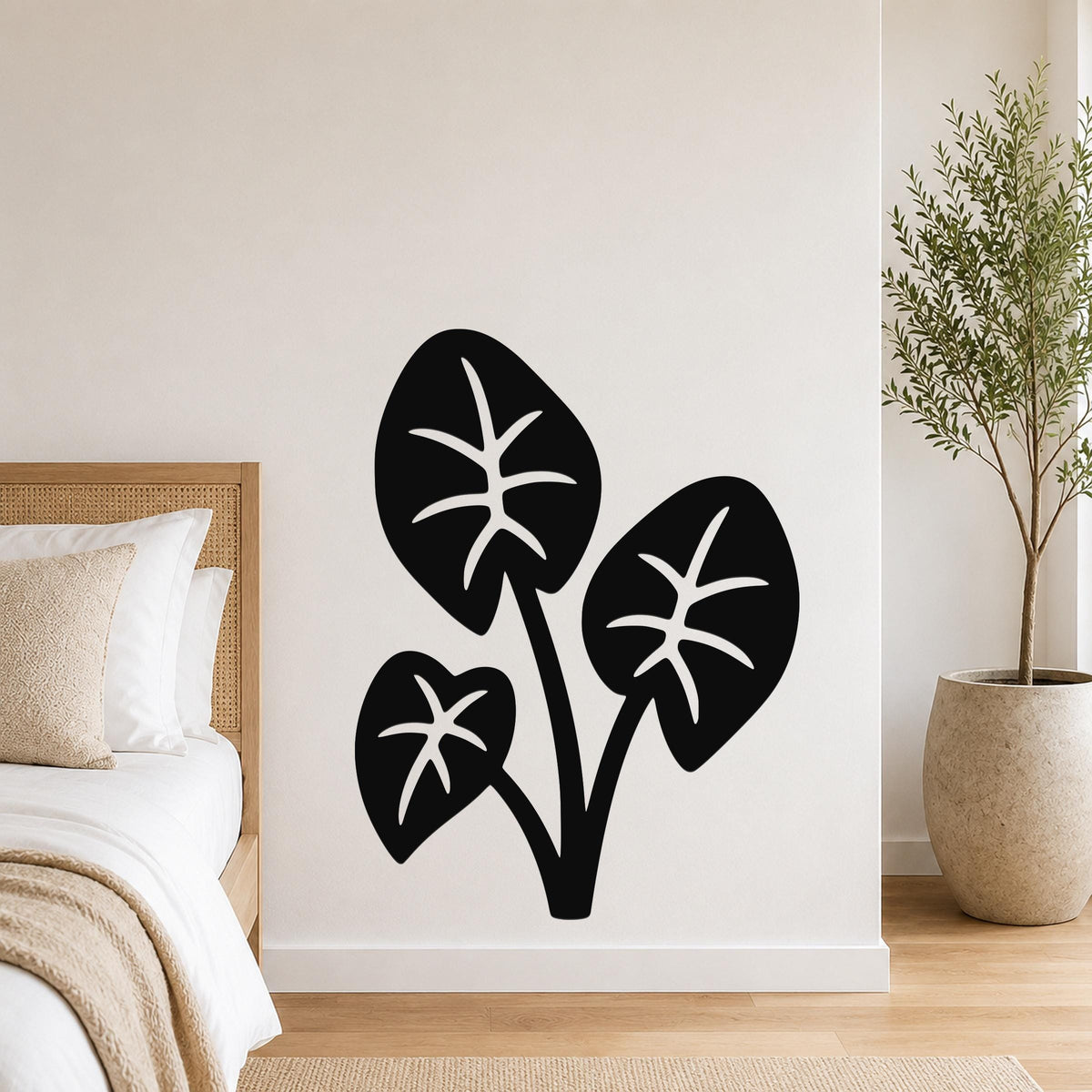 Black metal wall art featuring a cutout silhouette of three elephant ear leaves, mounted on a bedroom wall above a bed.