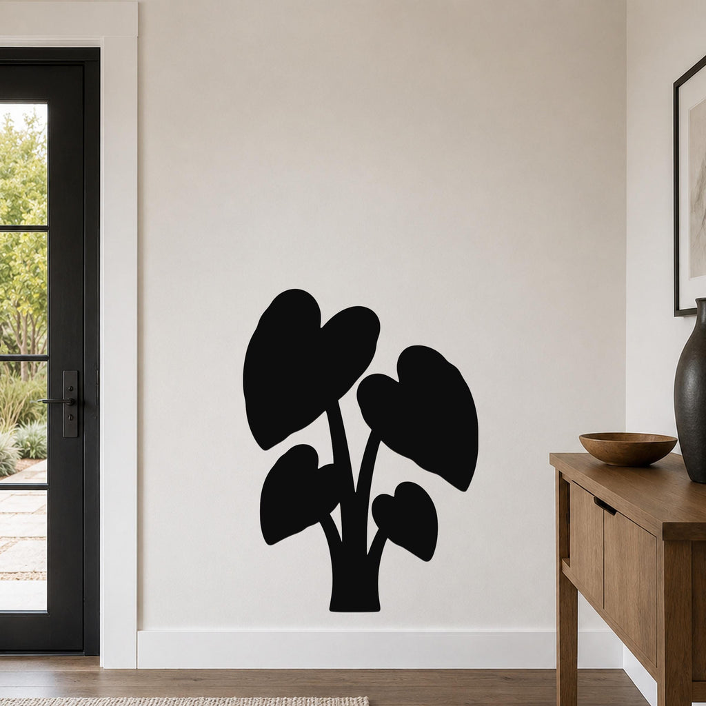 Black metal wall art in the silhouette of an elephant ear plant with large heart-shaped leaves, mounted on a living room wall above a wooden console table.