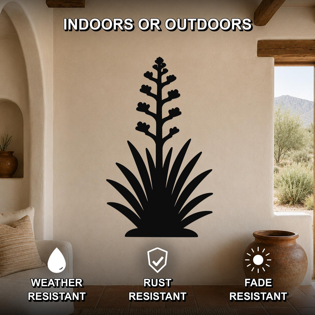 Black metal agave wall art with blooming flower cutout, mounted on a beige living room wall above a sofa, shown in an indoor setting with a desert view through a window.