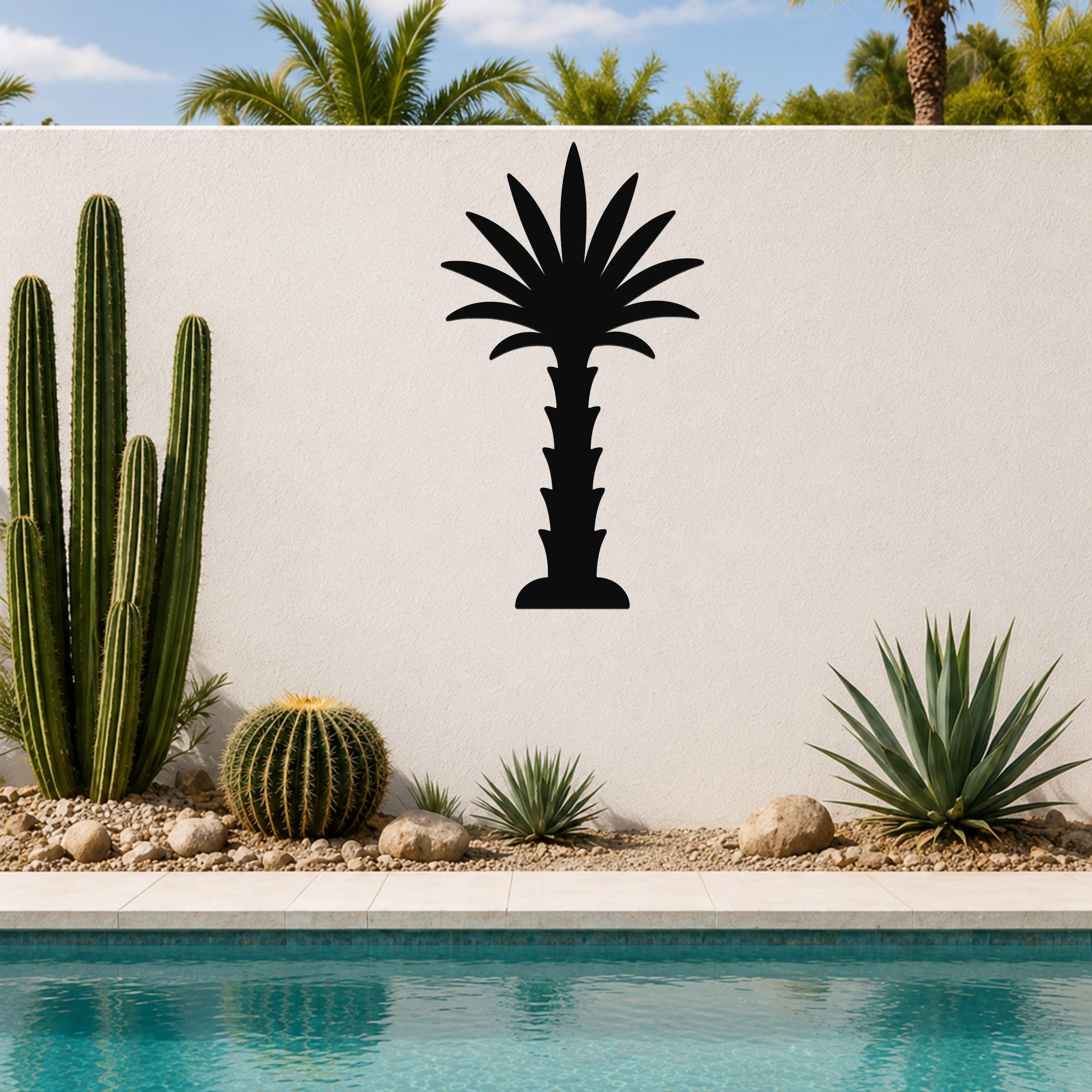 Black metal palm tree wall art silhouette mounted on a white outdoor wall above a pool, surrounded by cacti and desert plants.