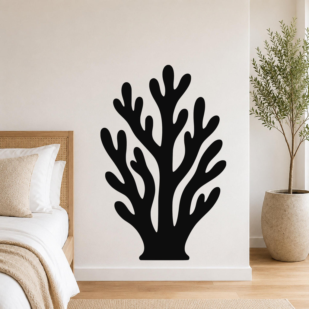 Black metal wall art in a branching coral silhouette, mounted on a bedroom wall above a bed with a woven headboard.
