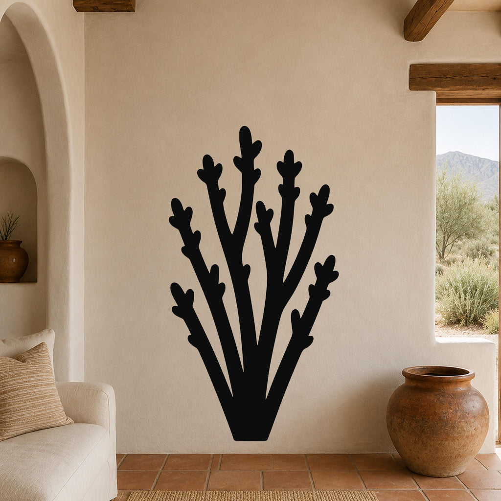 Black metal wall art in a desert branch silhouette, mounted on a beige stucco wall in a living room with terracotta flooring and wooden beams.