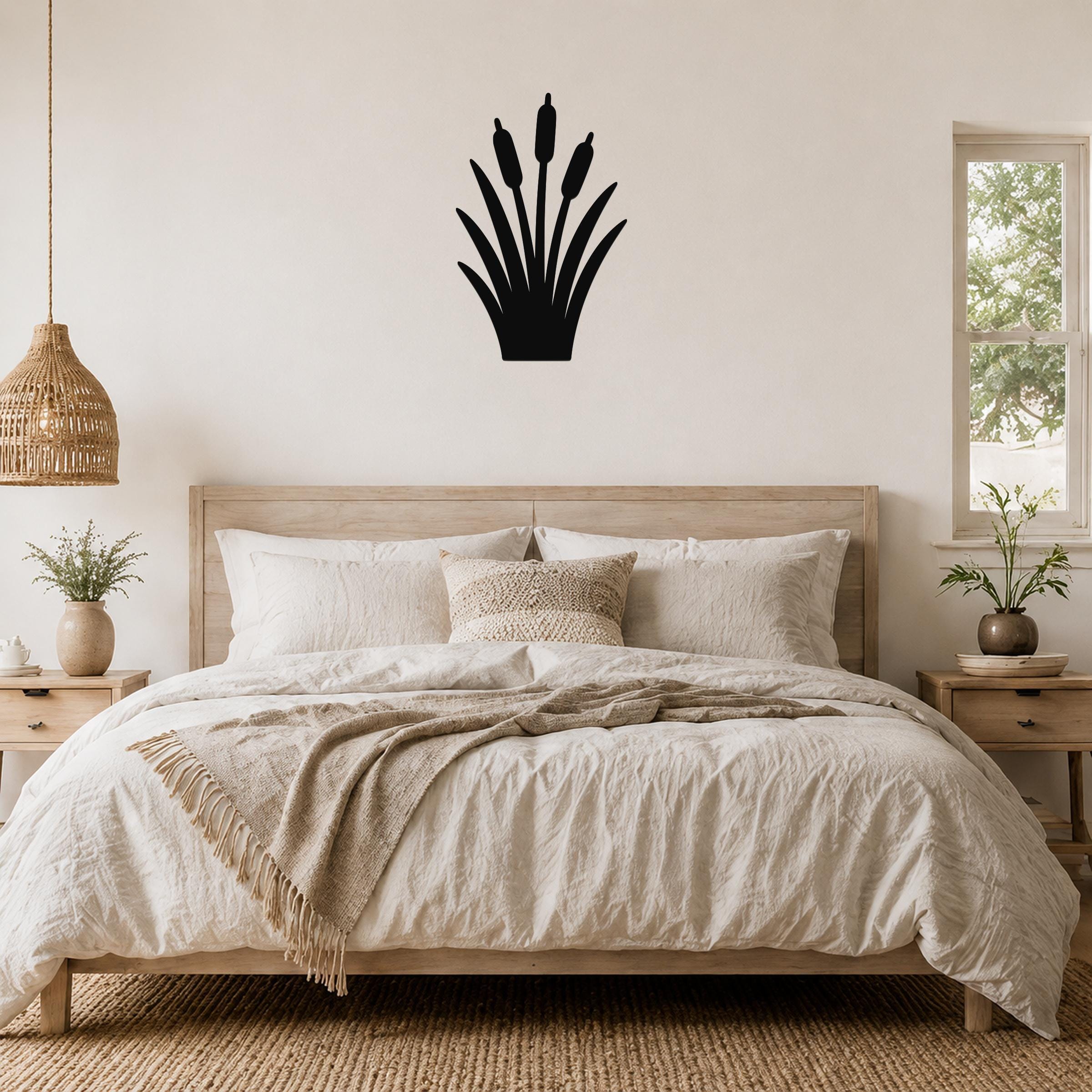 Black metal cattail wall art silhouette with three seed heads, mounted above a wooden bed in a neutral bedroom.