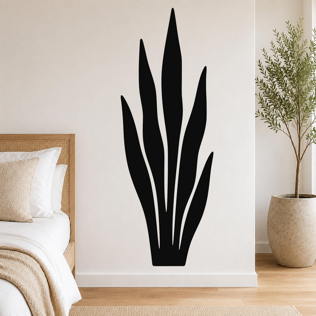 Black metal wall art in a snake plant silhouette, mounted on a white bedroom wall above a bed with a woven headboard.