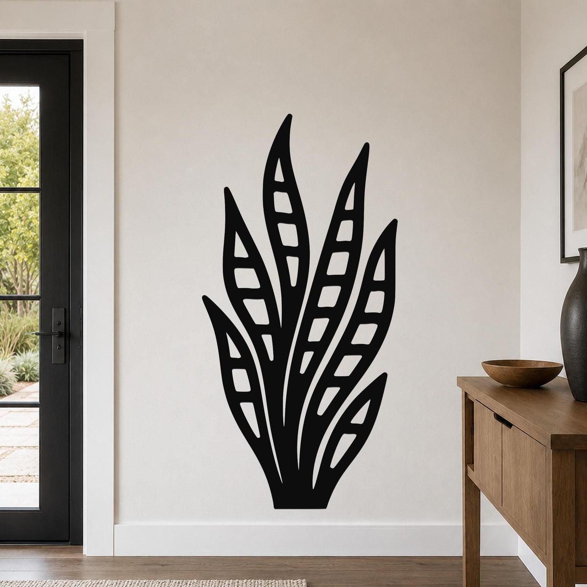 Black metal wall art in a snake plant silhouette with internal leaf cutouts, mounted on a living room wall above a wooden console table.