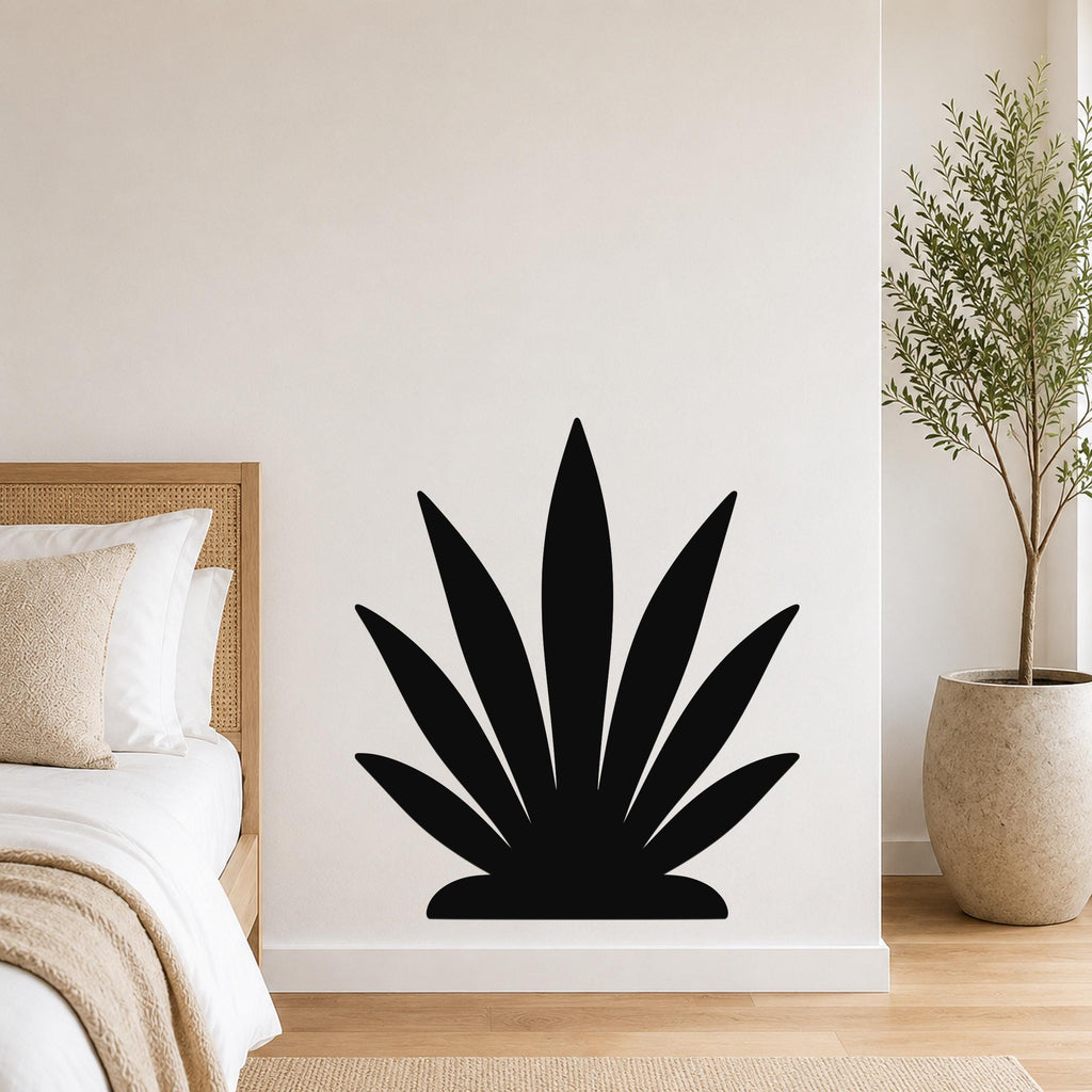 Black metal agave wall art silhouette mounted on a white bedroom wall above a bed with a woven headboard.