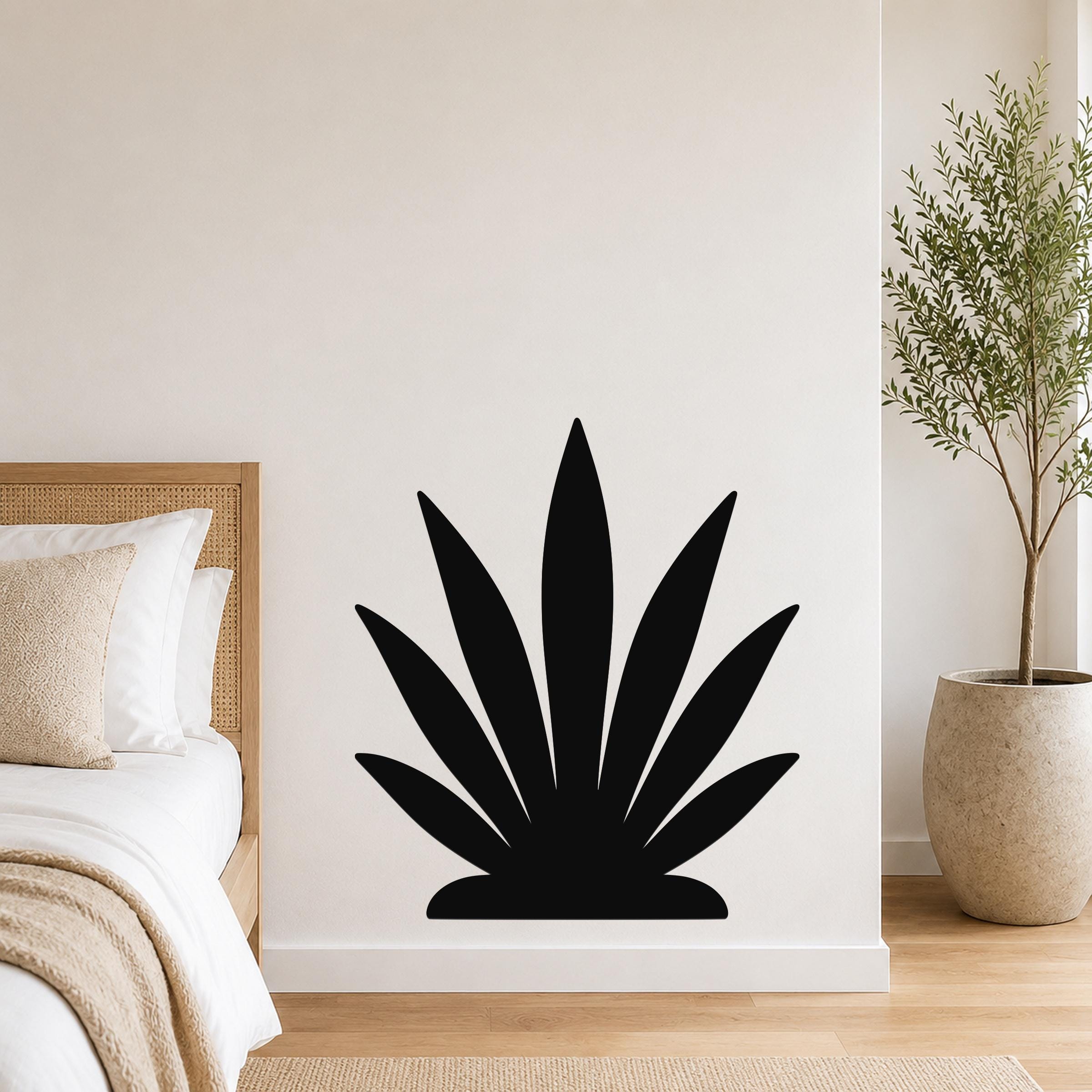 Black metal agave wall art silhouette mounted on a white bedroom wall above a bed with a woven headboard.