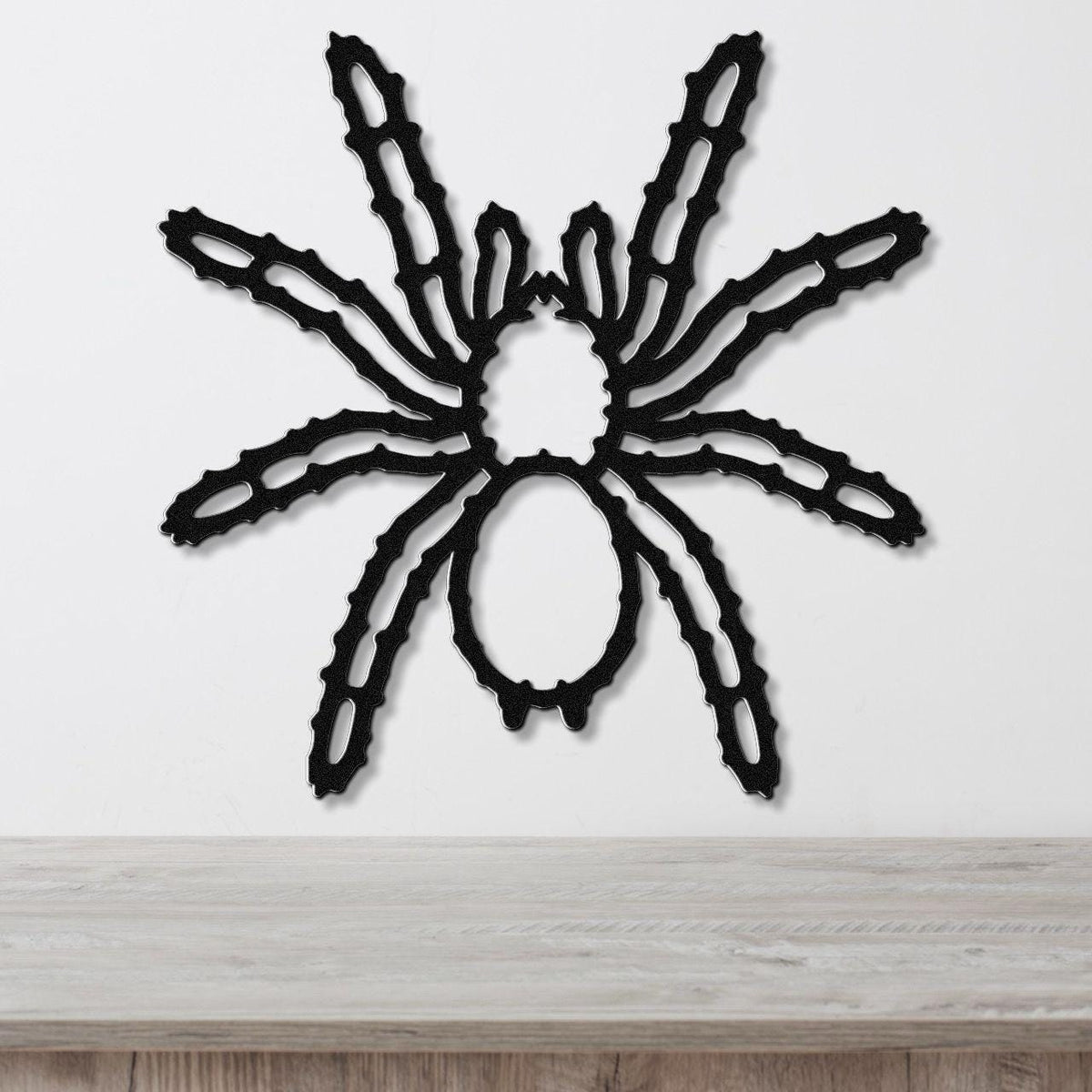 Black metal spider wall art with intricate leg cutouts, mounted on a white wall above a light wood surface.