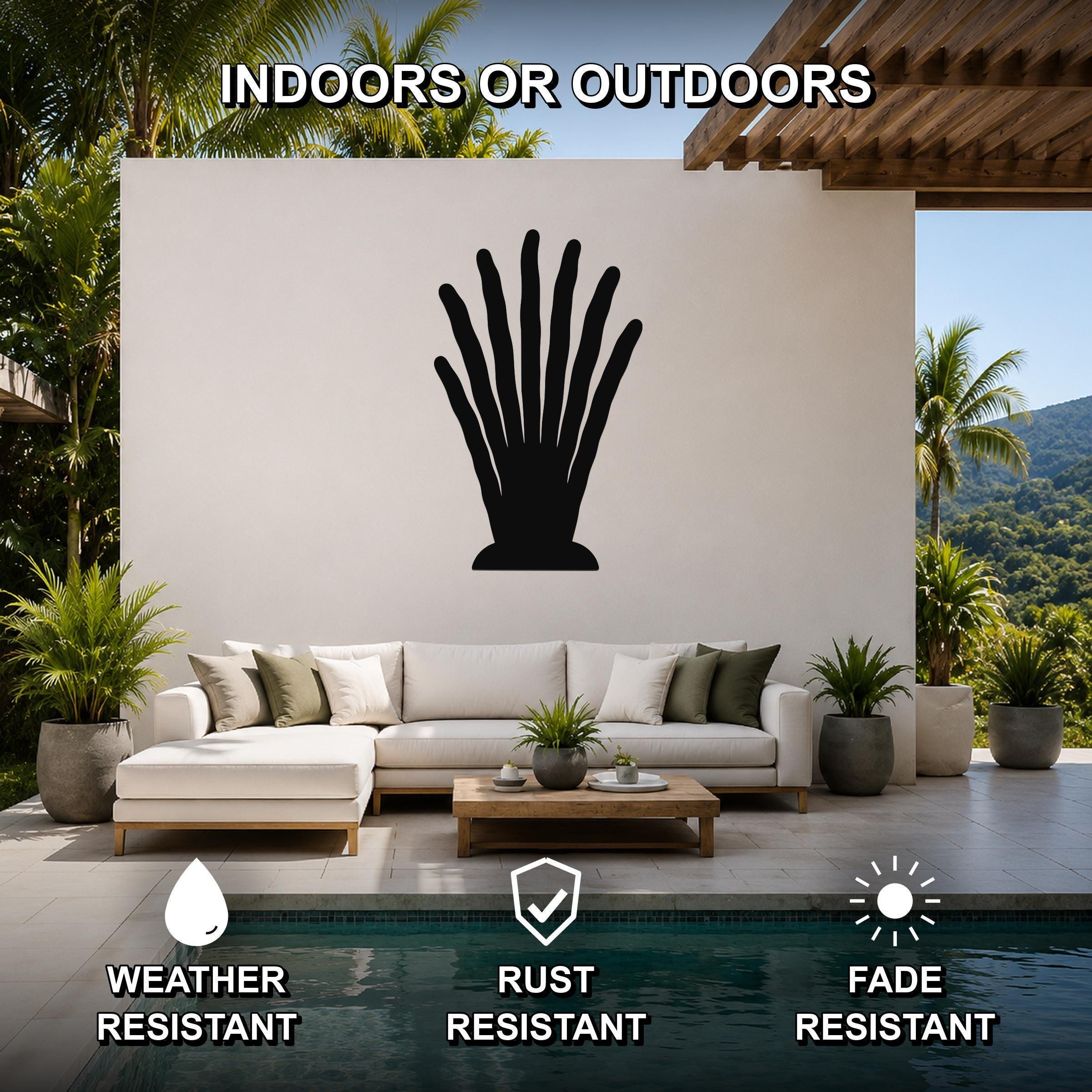 Black metal abstract plant wall art with radiating leaf cutouts, mounted on a white outdoor wall above a sofa in a patio living area.
