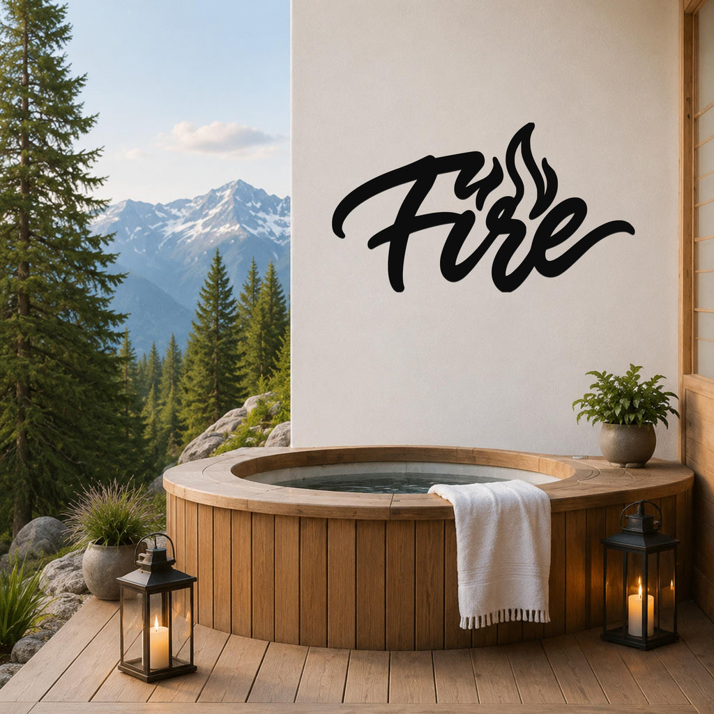 Black metal wall art with the word "Fire" in cursive script and flame cutouts, mounted on a white wall above a wooden hot tub on a deck with mountain views.