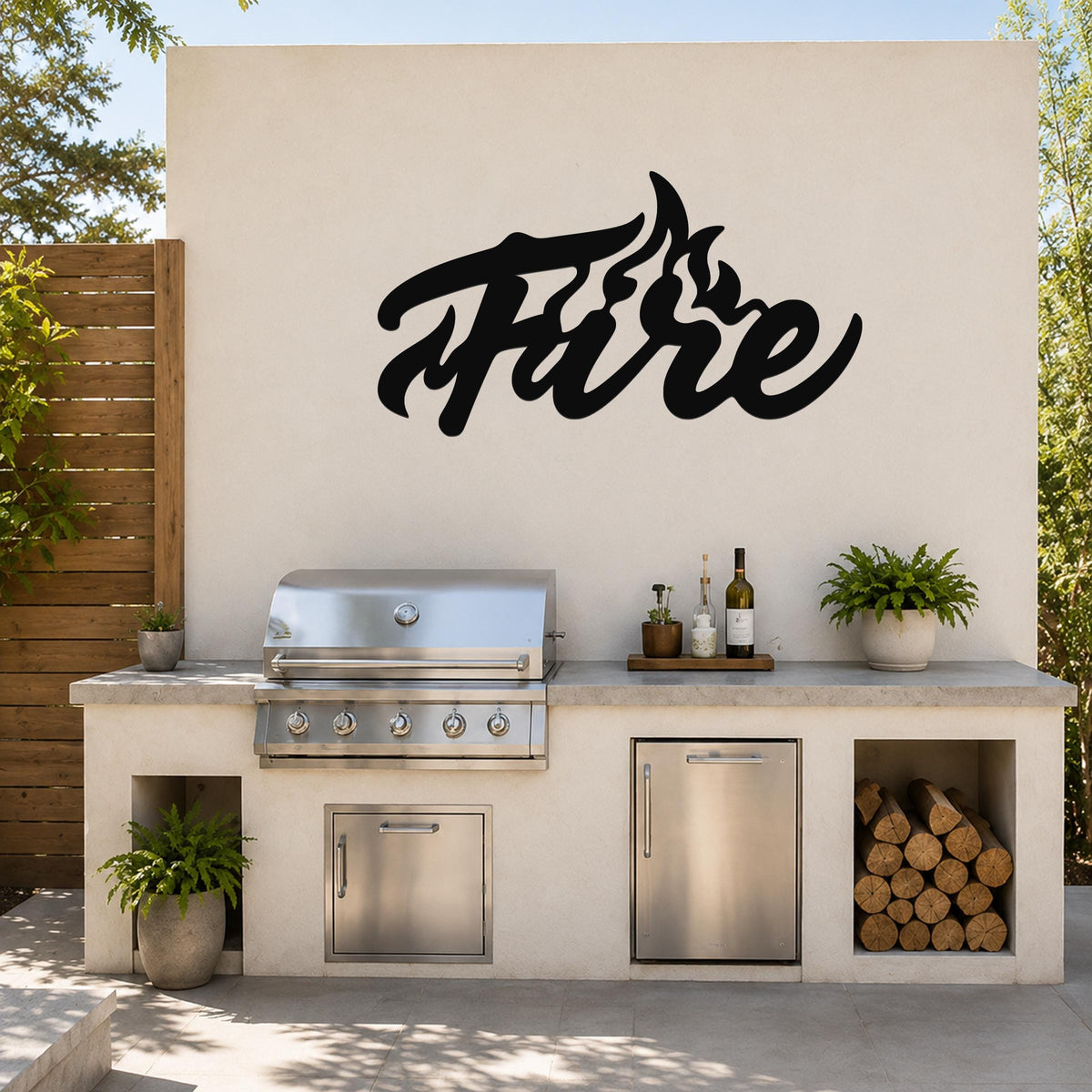 Black metal wall art with a stylized "Fire" script and flame cutouts, mounted on an outdoor kitchen wall above a stainless steel grill and counter.