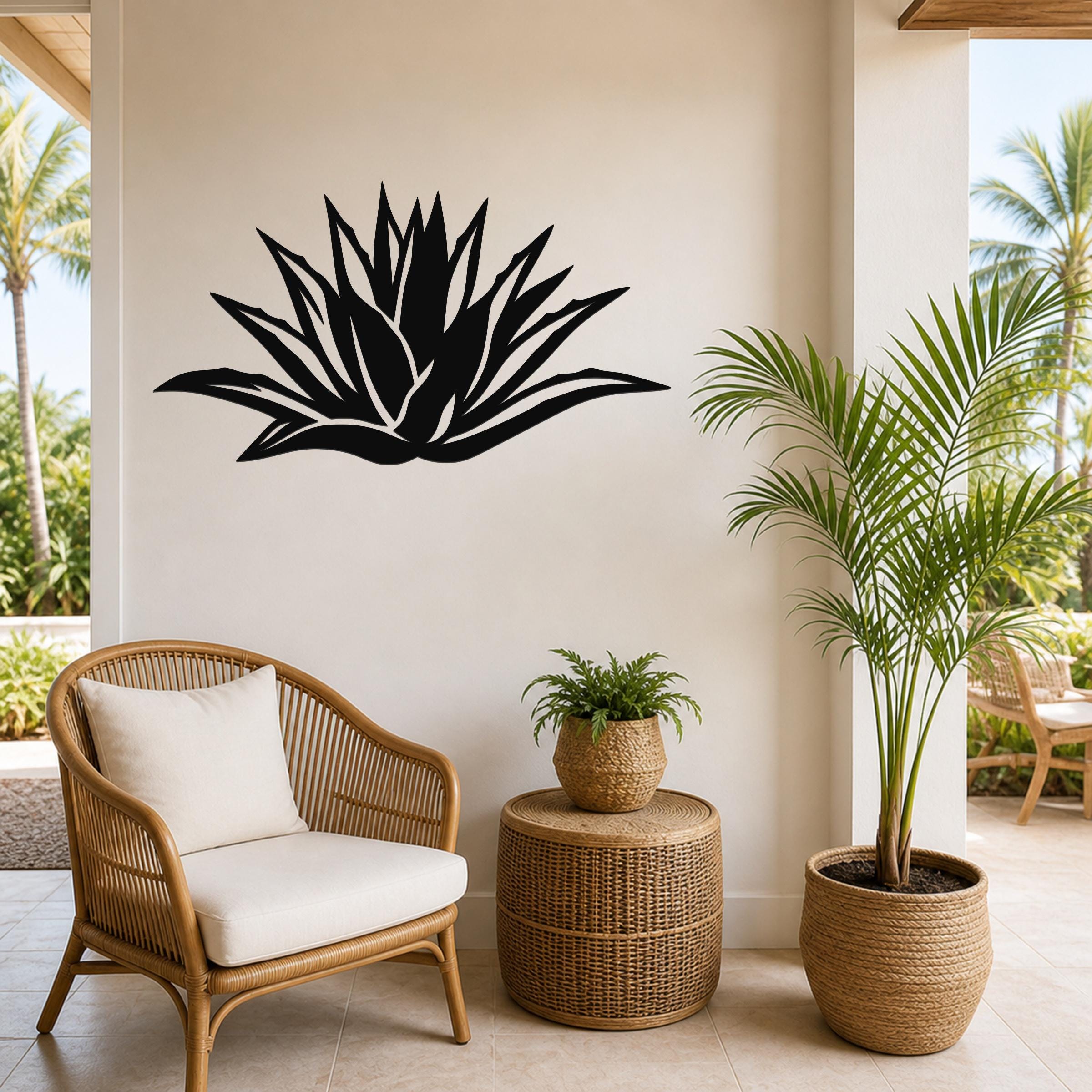 Black metal agave wall art with leaf cutouts, mounted on a light-colored wall above a wicker chair and potted plants on a covered patio.