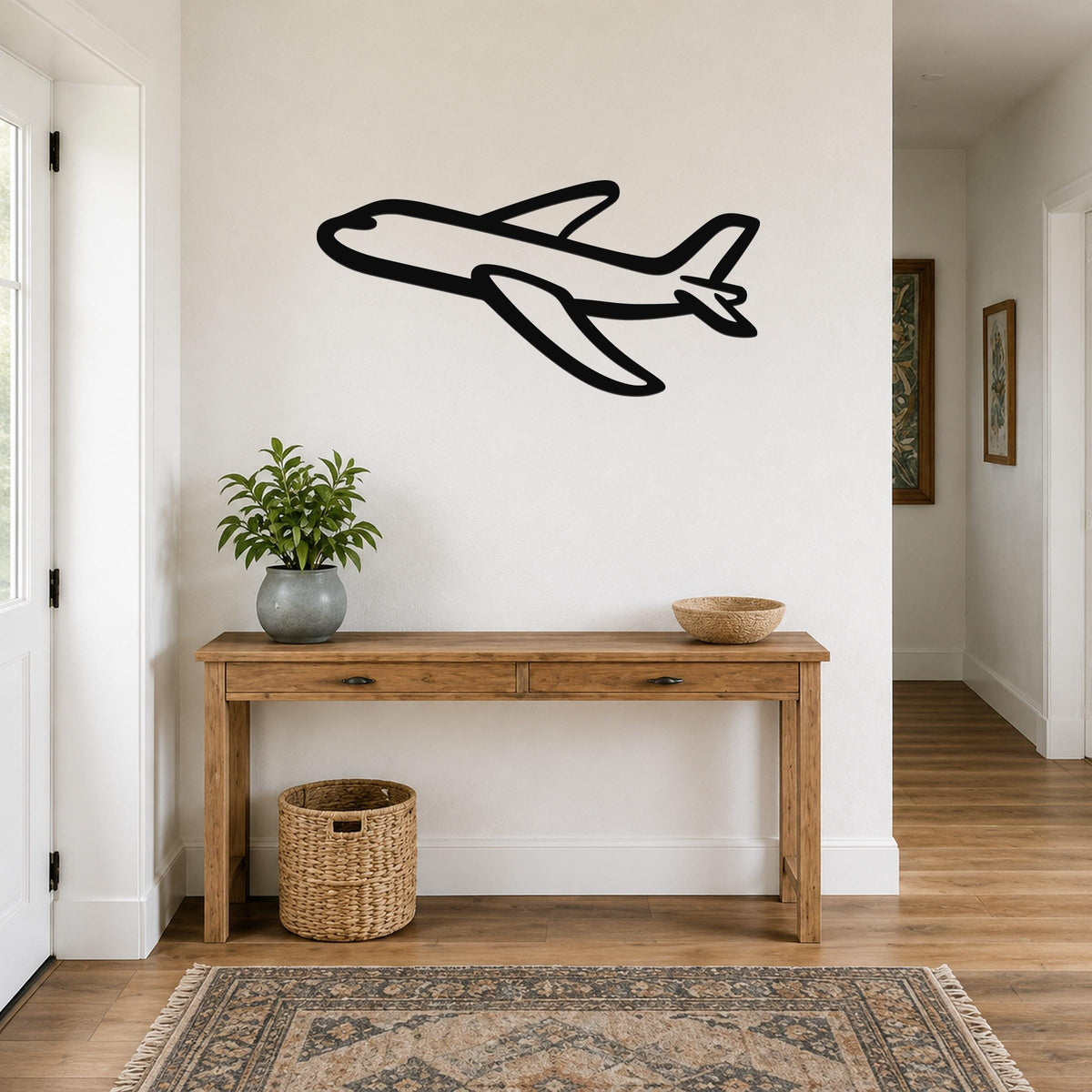 Black metal airplane wall art with a bold silhouette design, mounted on a white wall above a wooden console table in a hallway.