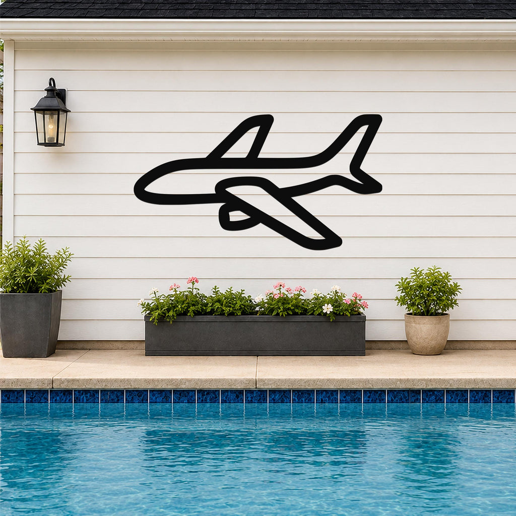 Black metal airplane wall art silhouette mounted on a white horizontal siding wall above a poolside planter with flowers and plants.