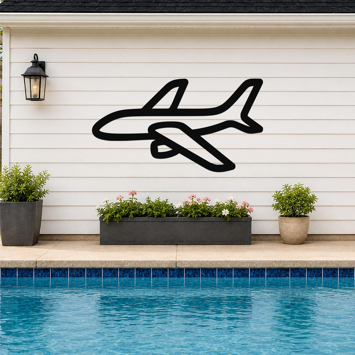 Black metal airplane wall art silhouette mounted on a white horizontal siding wall above a poolside planter with flowers and plants.
