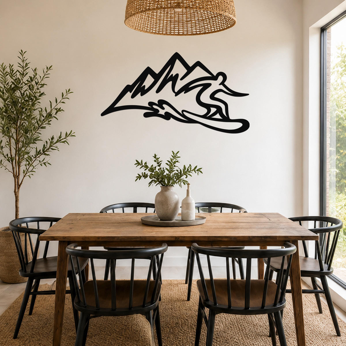 Black metal wall sculpture of a snowboarder in motion above a mountain range, mounted on a dining room wall above a wooden table.