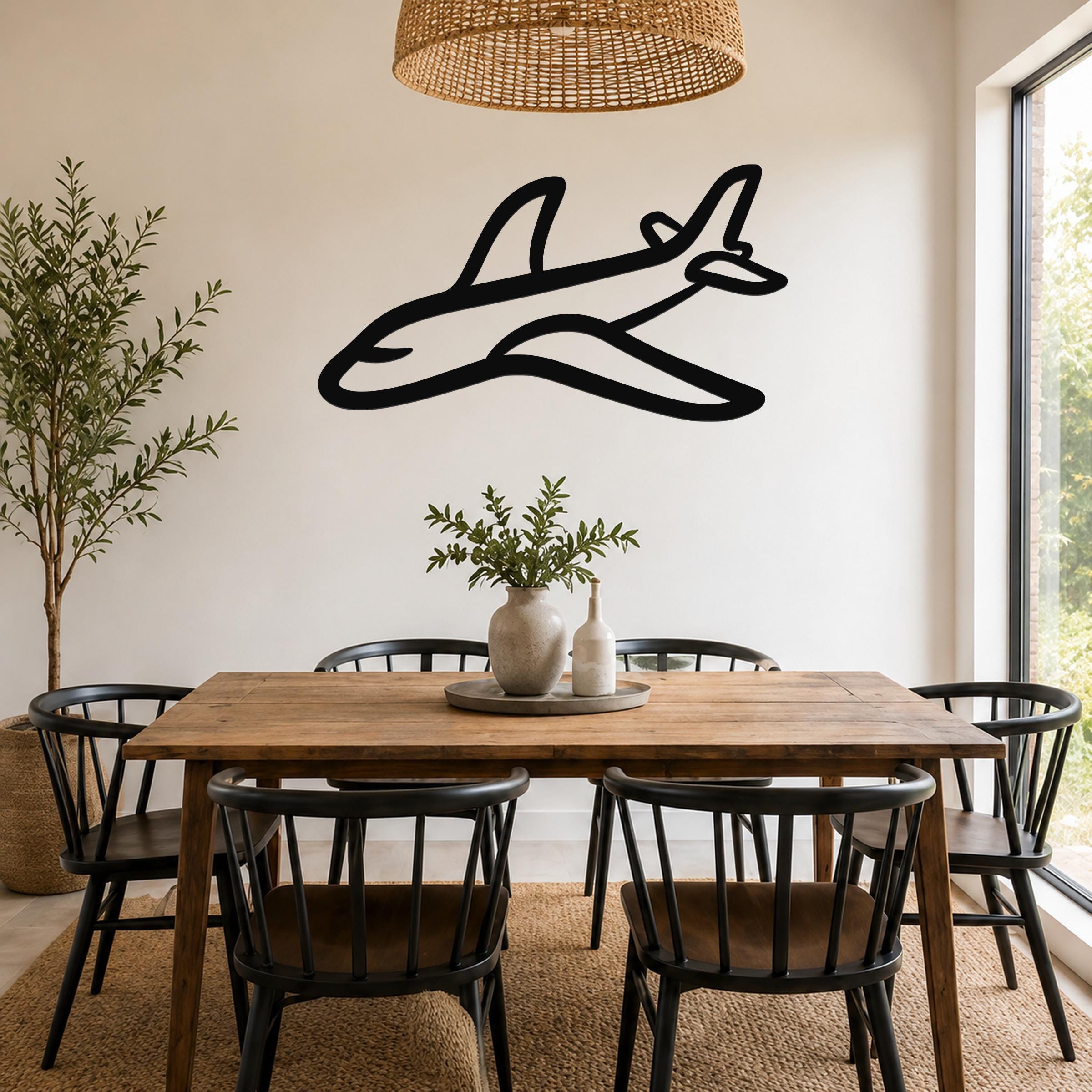Black metal airplane wall art silhouette mounted on a white wall above a wooden dining table in a bright dining room.