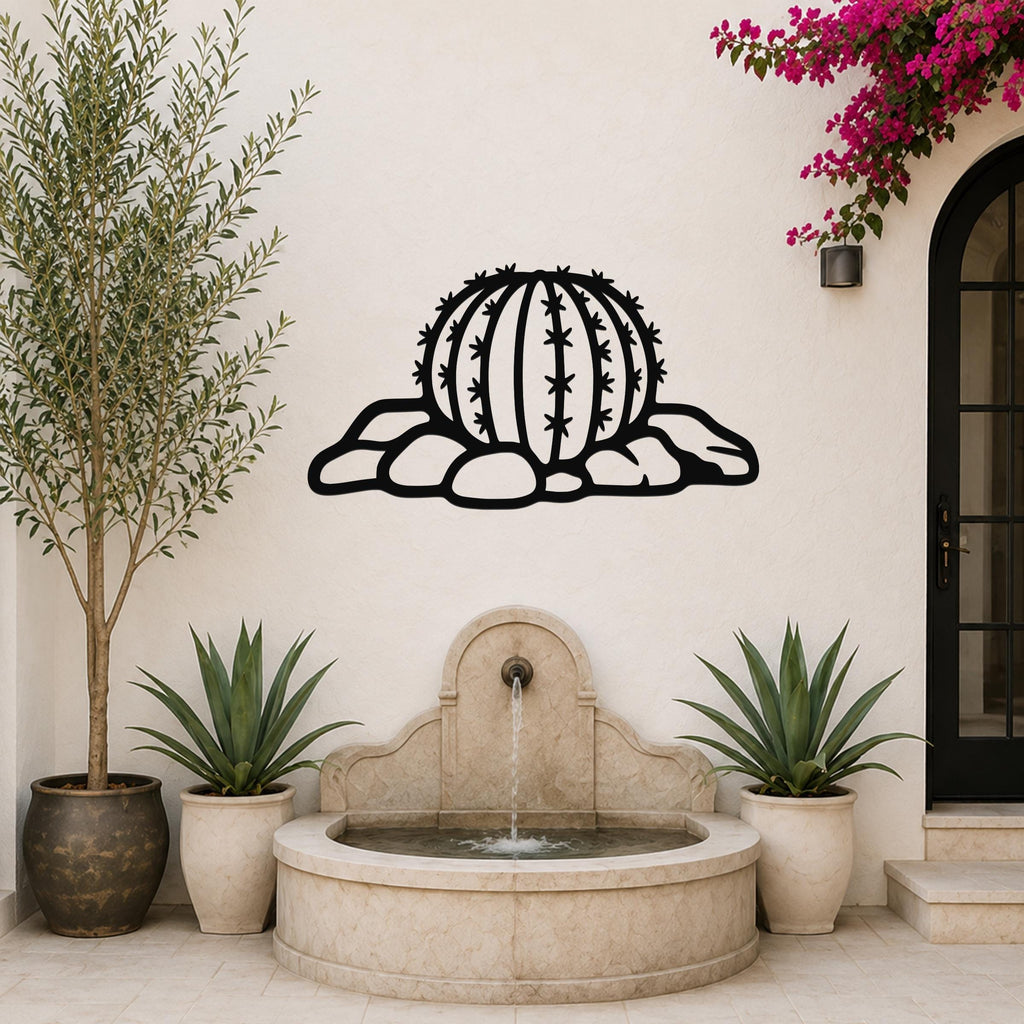 Black metal barrel cactus wall art with spines and rocks cutout, mounted on a white outdoor wall above a stone fountain.