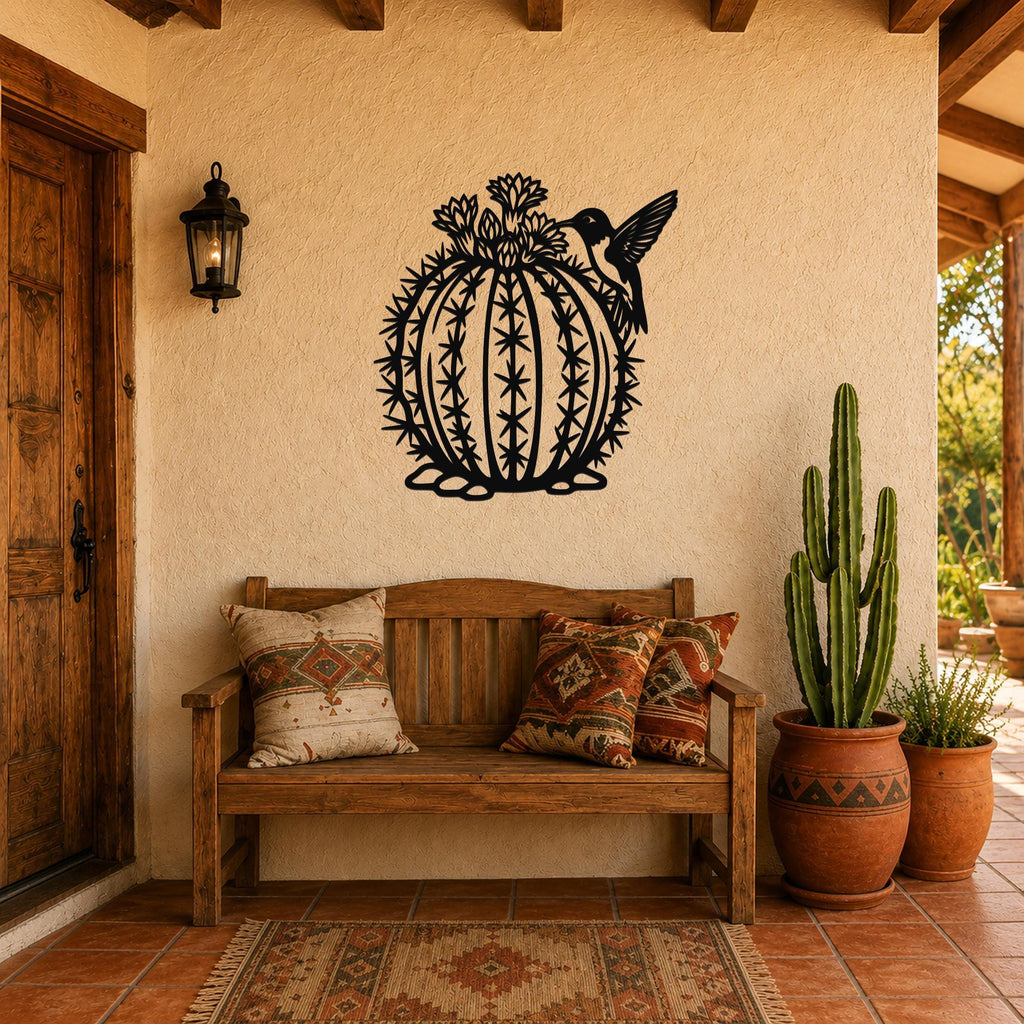 Black metal barrel cactus wall art with hummingbird and flower cutouts, mounted on a stucco wall above a wooden bench in a patio entryway.