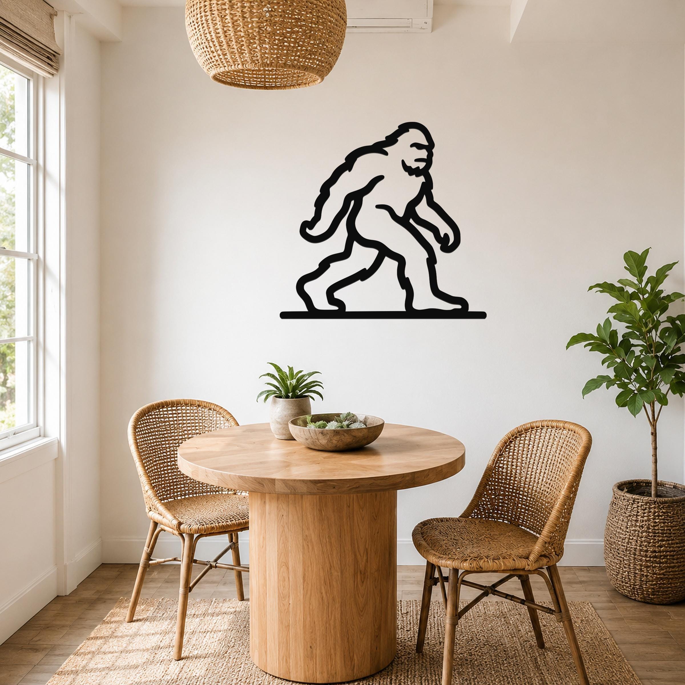 Black metal Bigfoot wall art silhouette mounted on a white wall above a round wooden table in a bright dining area.