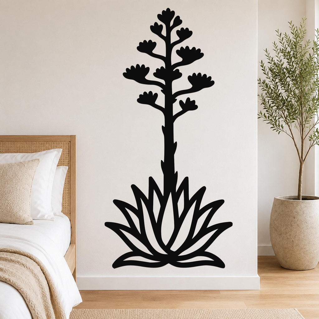 Black metal wall art silhouette of a blooming agave plant with a tall flower stalk and rosette base, mounted on a bedroom wall above a bed.