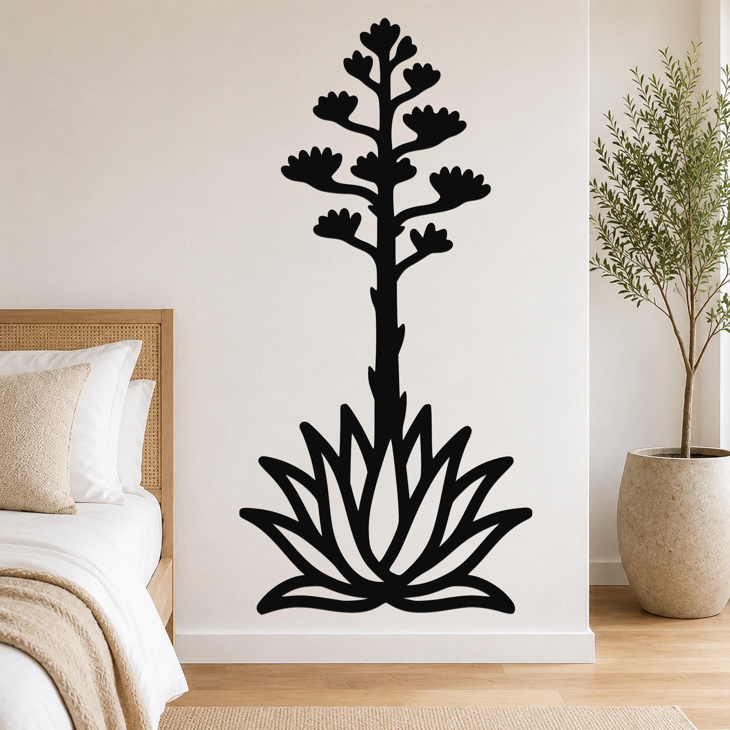 Black metal wall art silhouette of a blooming agave plant with a tall flower stalk and rosette base, mounted on a bedroom wall above a bed.