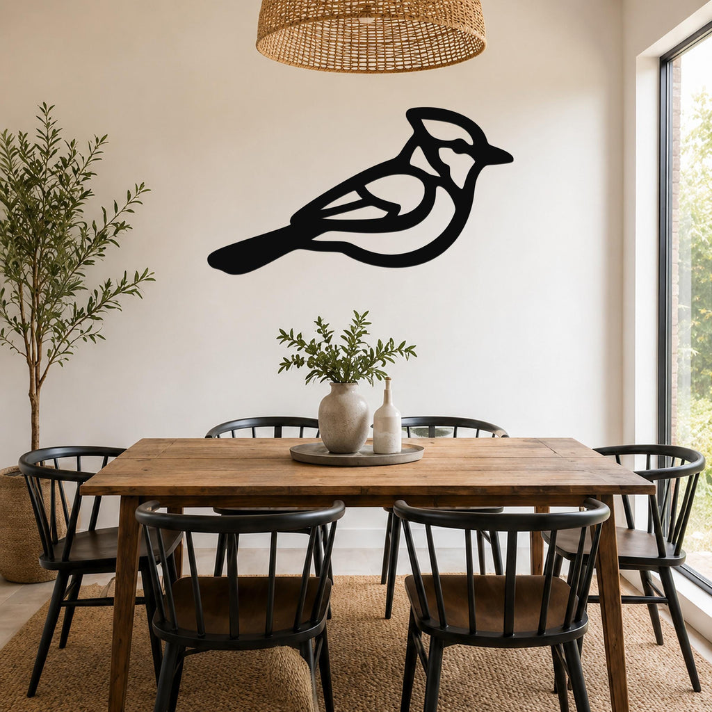 Black metal bird wall art with internal cutout details, mounted on a white wall above a wooden dining table in a bright dining room.