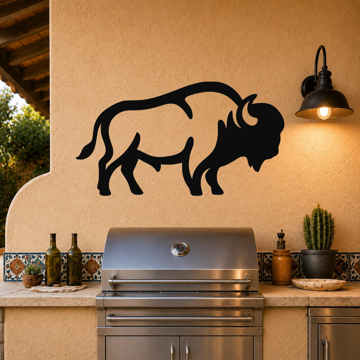 Black metal bison silhouette wall art mounted on a stucco wall above a stainless steel grill in an outdoor kitchen.