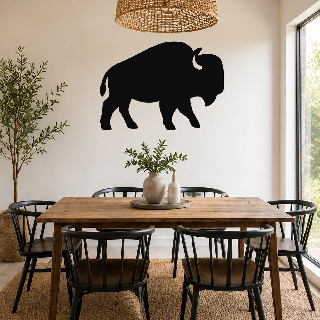 Black metal buffalo wall art silhouette mounted on a white wall above a wooden dining table in a bright, modern dining room.