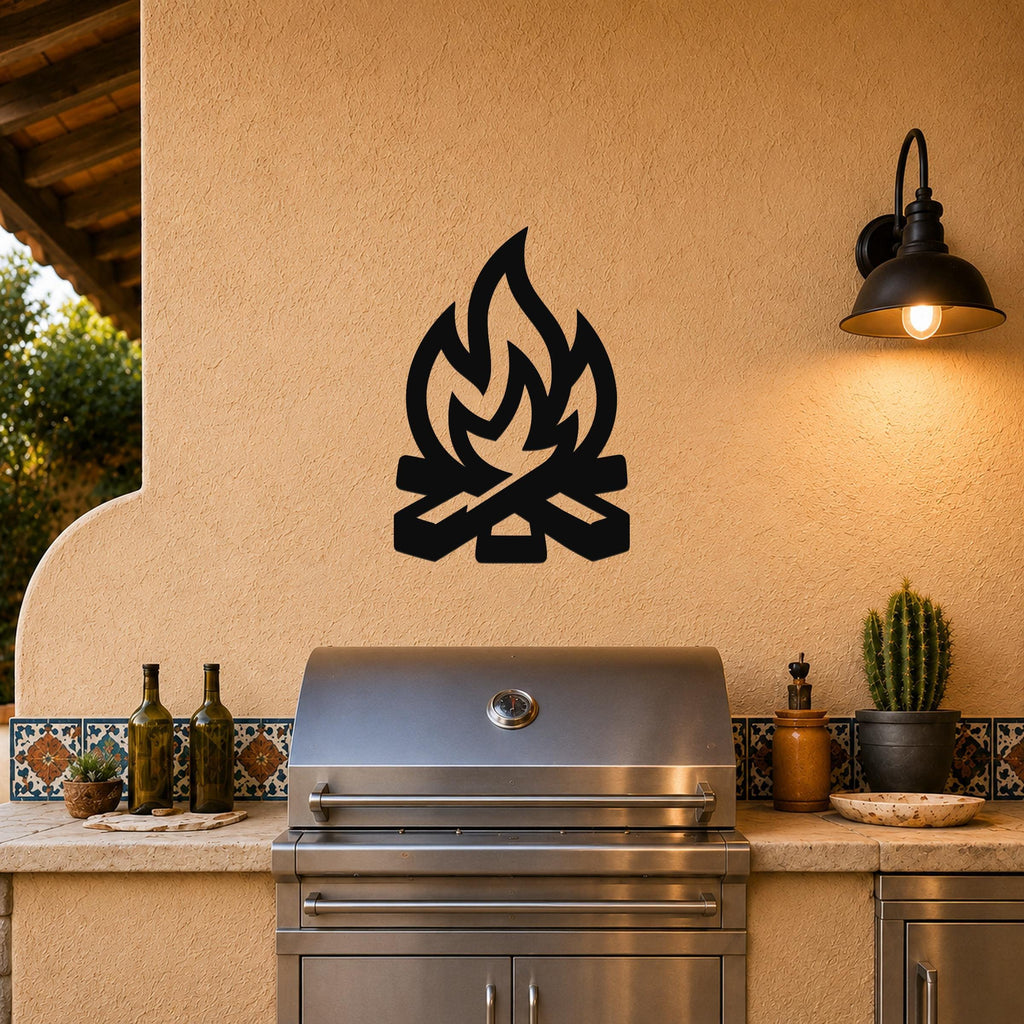 Black metal campfire wall art with flame and log silhouette, mounted on a stucco wall above a stainless steel grill on an outdoor patio.