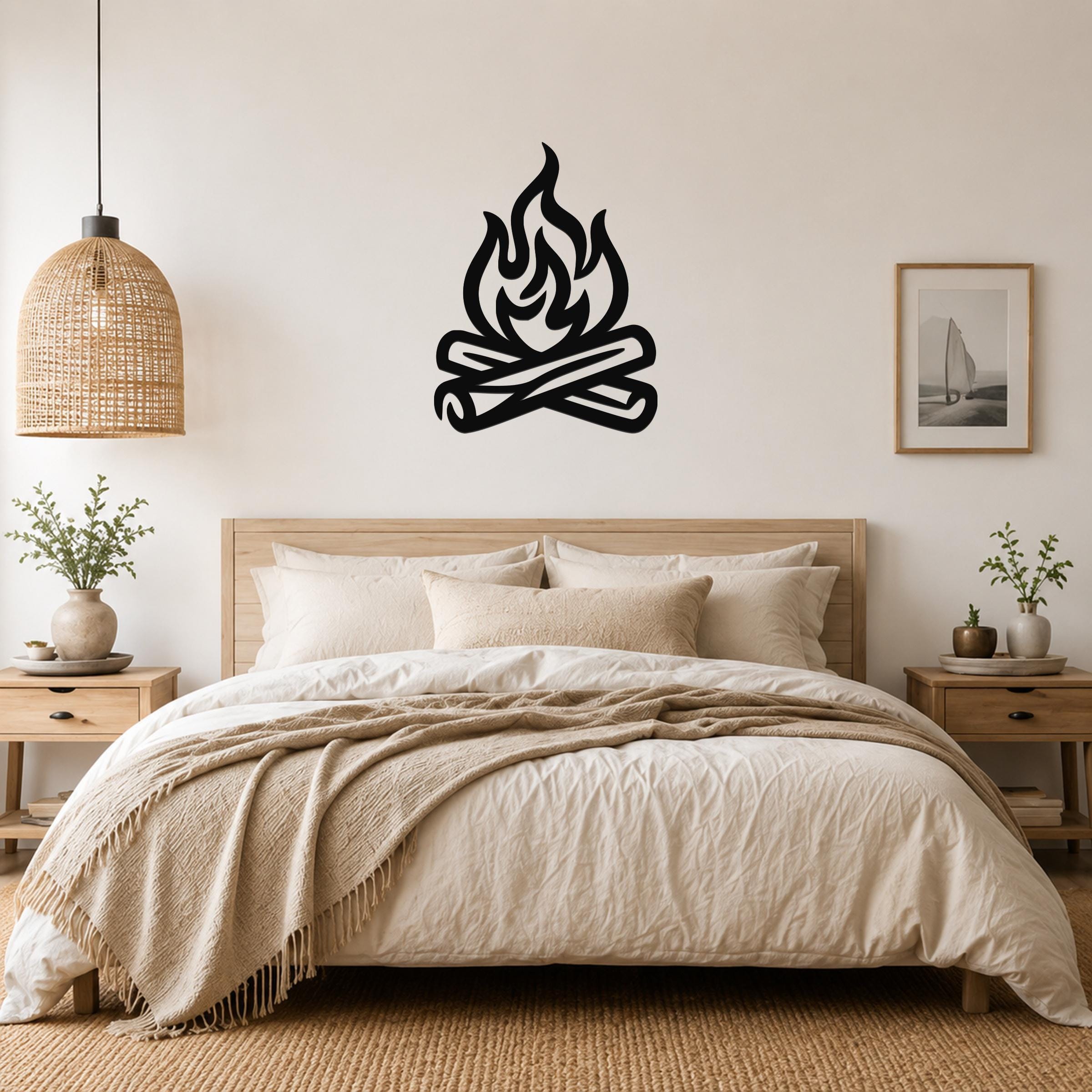 Black metal campfire wall art with flame and log silhouette, mounted above a bed in a neutral bedroom.