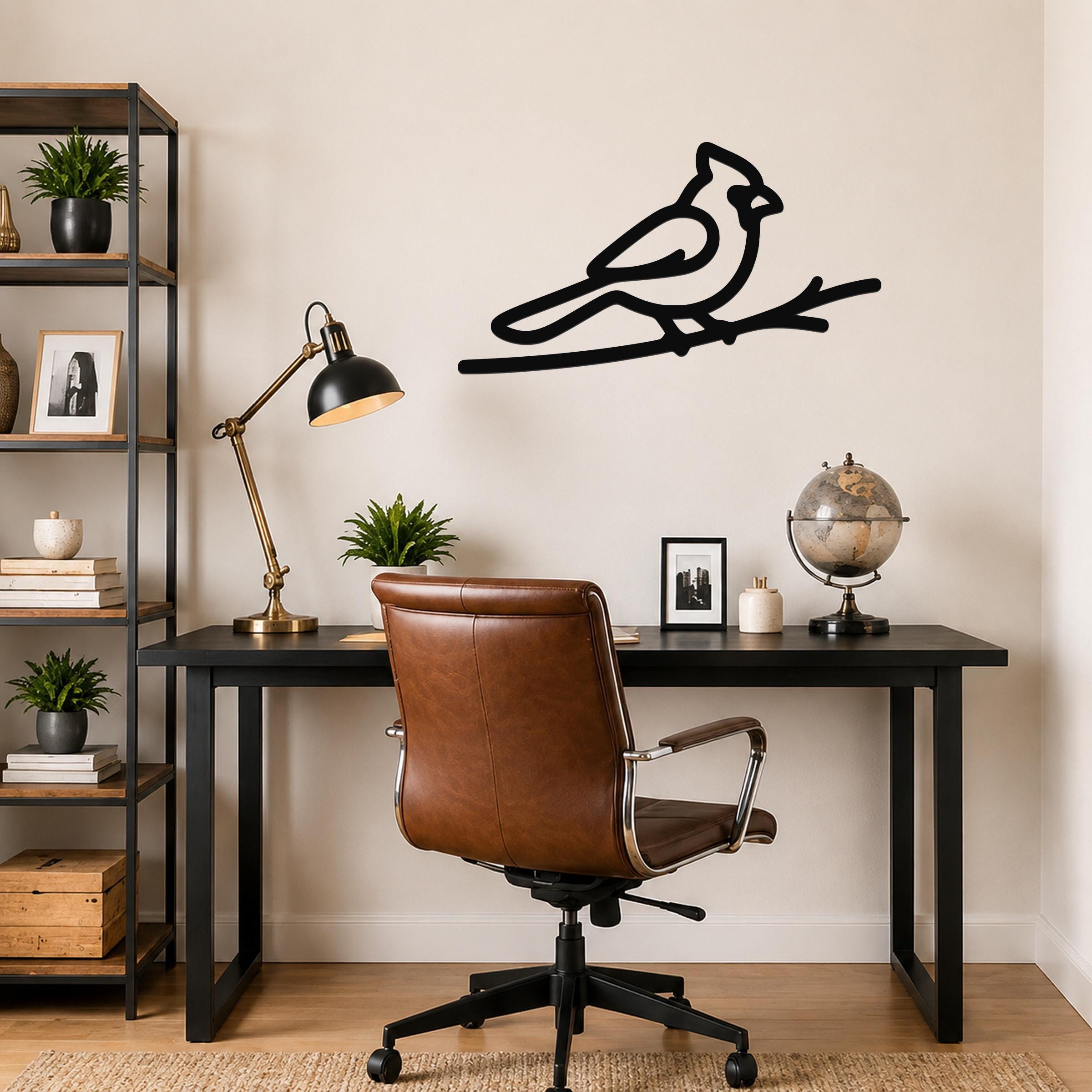 Black metal cardinal wall art in a minimalist silhouette, perched on a branch, mounted above a black desk in a home office.