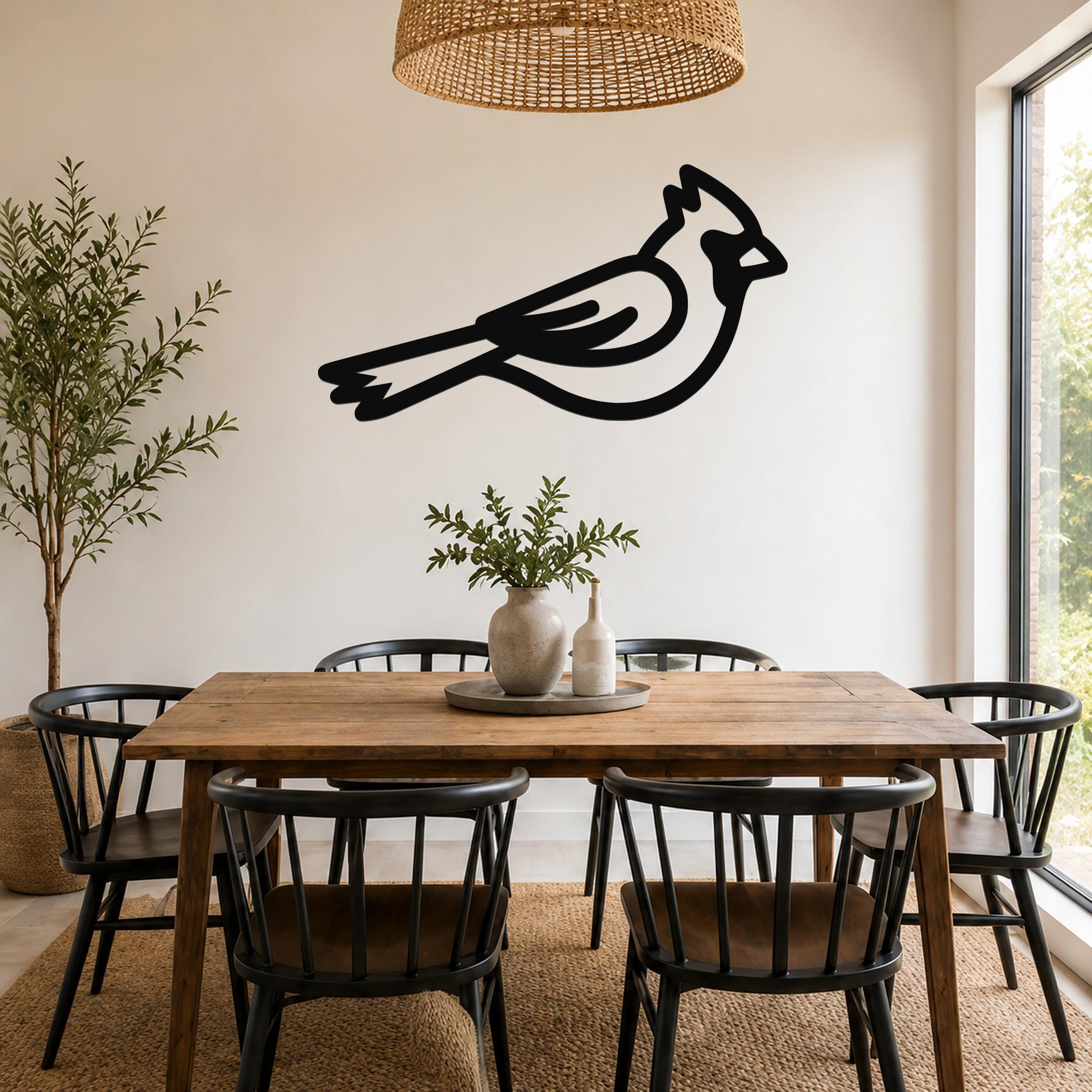 Black metal cardinal wall art silhouette mounted on a white wall above a wooden dining table in a bright room.