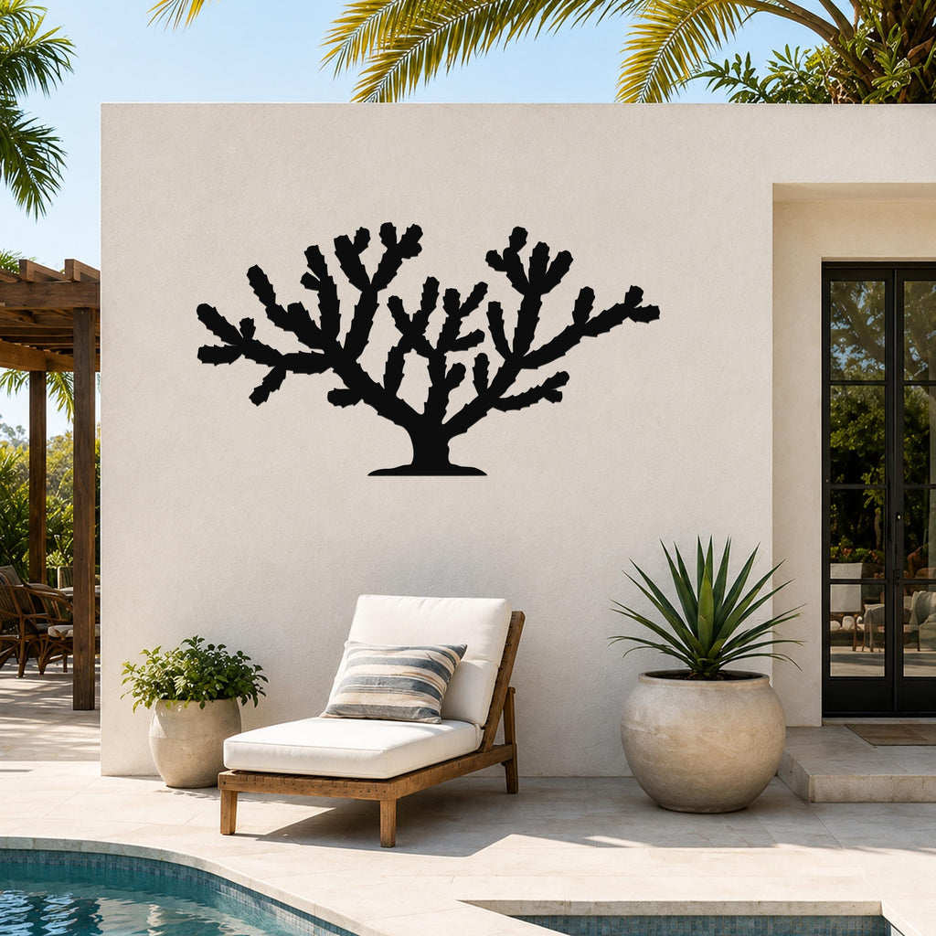 Black metal Cholla cactus wall art silhouette mounted on an outdoor patio wall above a lounge chair and potted plants.