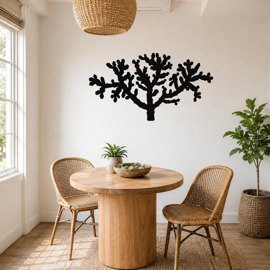 Black metal cholla cactus wall art with branching cutouts, mounted on a white wall above a round wooden table in a bright dining nook.