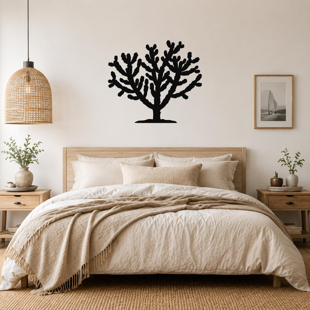 Black metal Cholla cactus wall art silhouette with branching arms, mounted above a wooden bed in a neutral bedroom.
