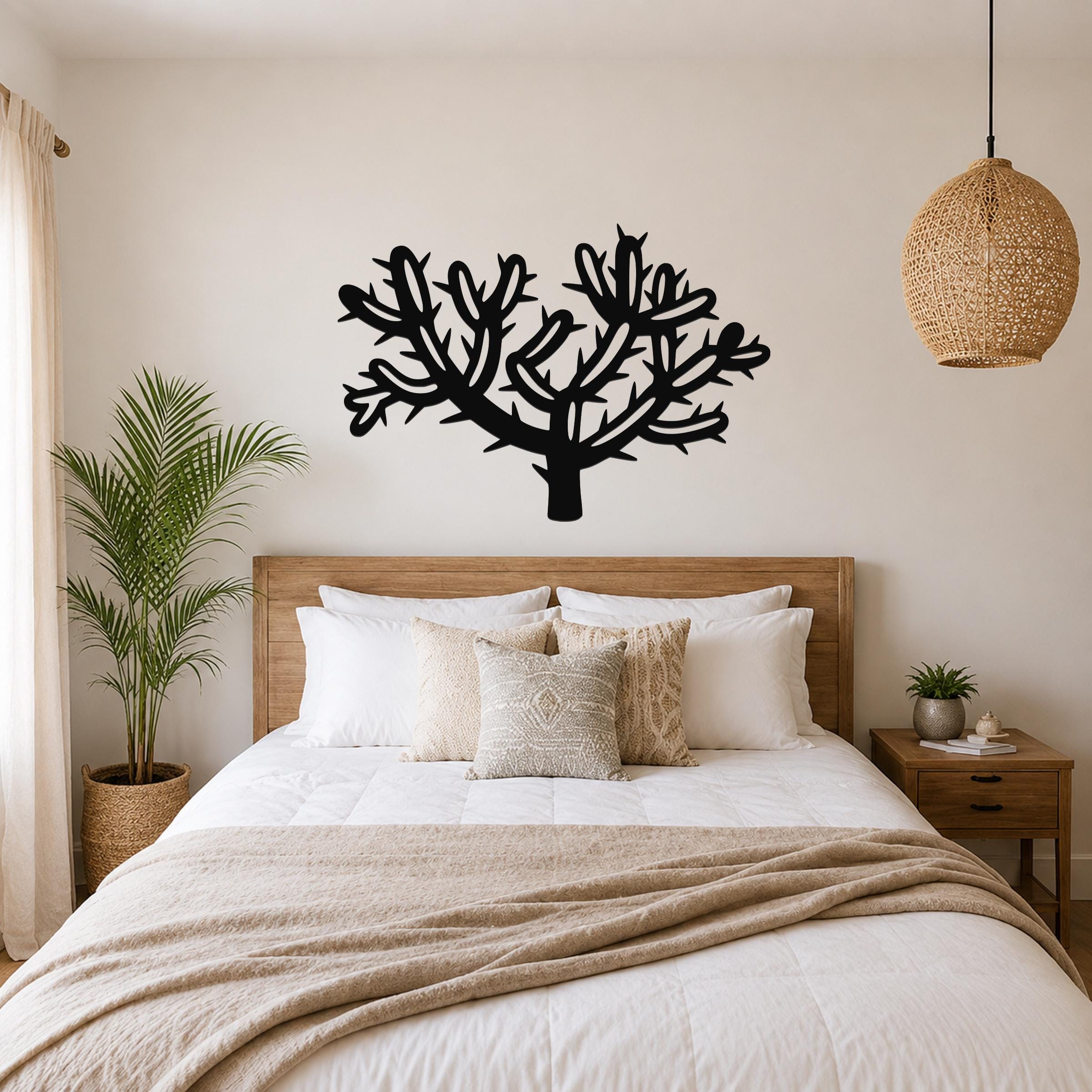 Black metal cholla cactus wall art with branching cutouts, mounted above a wooden bed in a neutral bedroom.