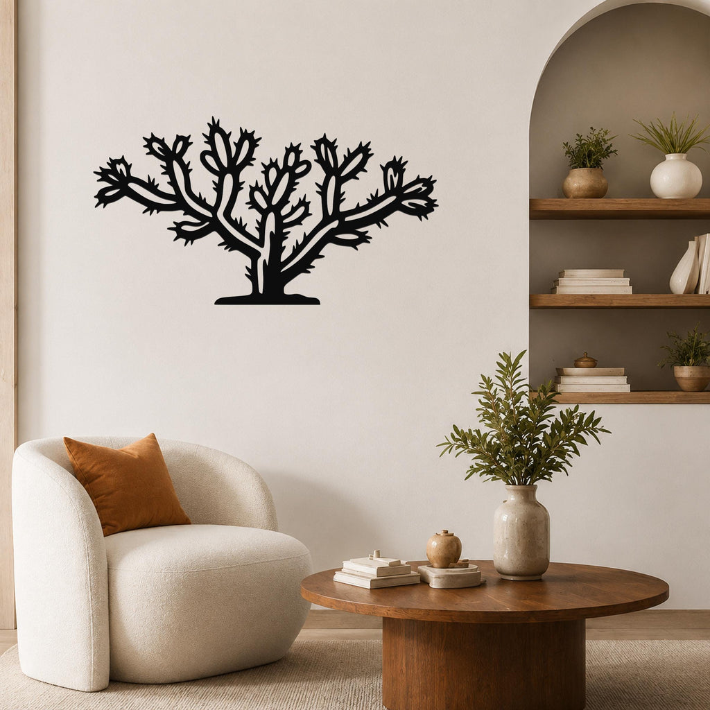 Black metal cholla cactus wall art with branching spines and cutout details, mounted on a living room wall above a round wooden coffee table.
