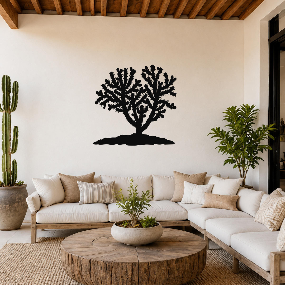 Black metal Cholla cactus wall art silhouette with branching spines, mounted on a living room wall above a white sofa.