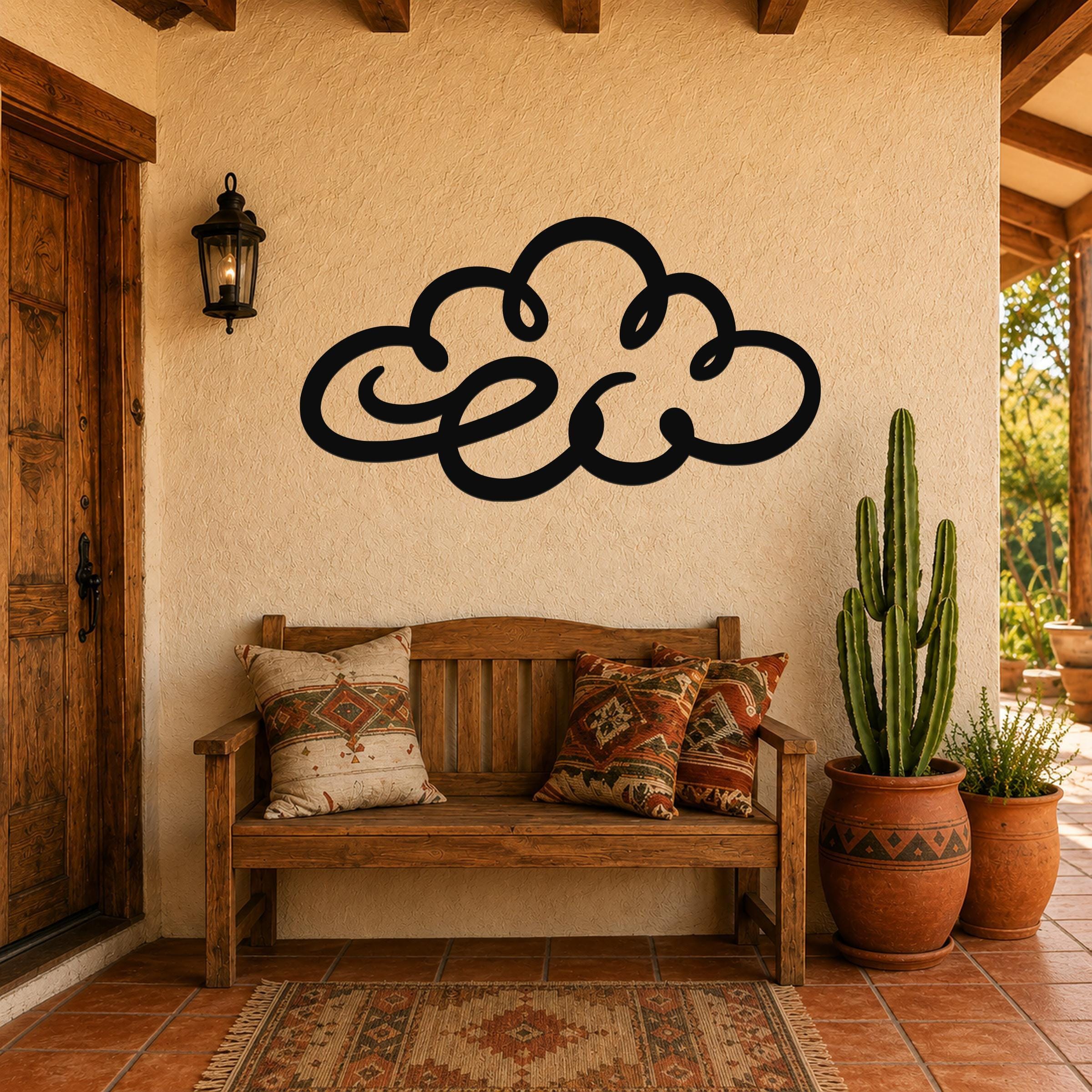 Black metal cloud wall art with flowing silhouette cutouts, mounted on a stucco wall above a wooden bench in a patio entryway.